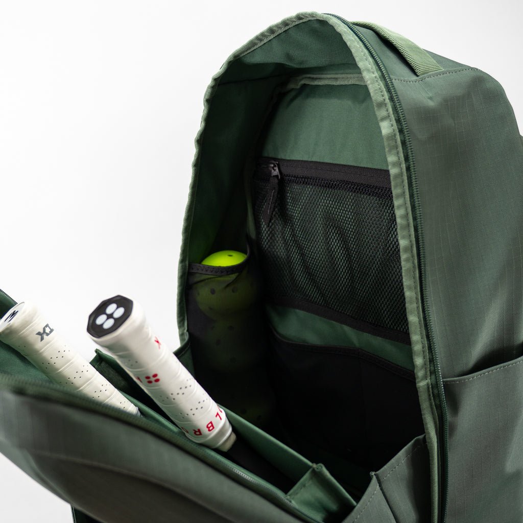 Dark green pickleball backpack by FORWRD, open to reveal pickleball paddles, bright yellow balls, and internal mesh pockets.