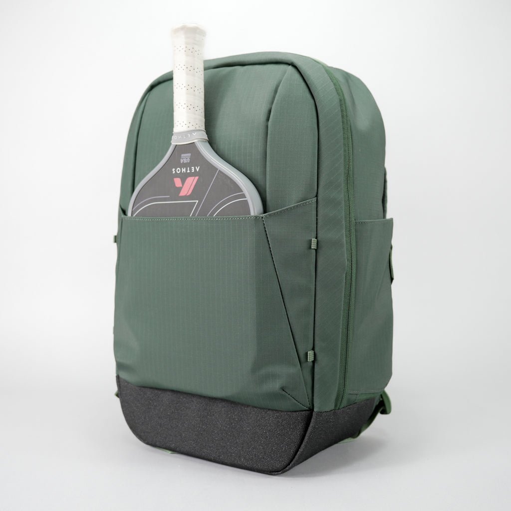 Green textured Pickleball Backpack by FORWRD, with a grey paddle and white grip in the front pocket and a dark grey base.