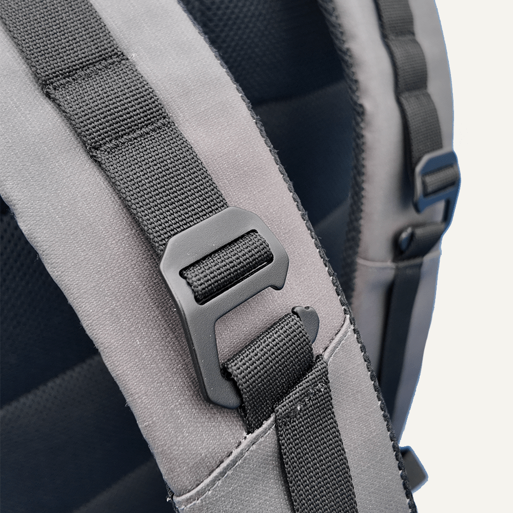 Close-up of a gray backpack shoulder strap with black webbing and a black metal clip.
