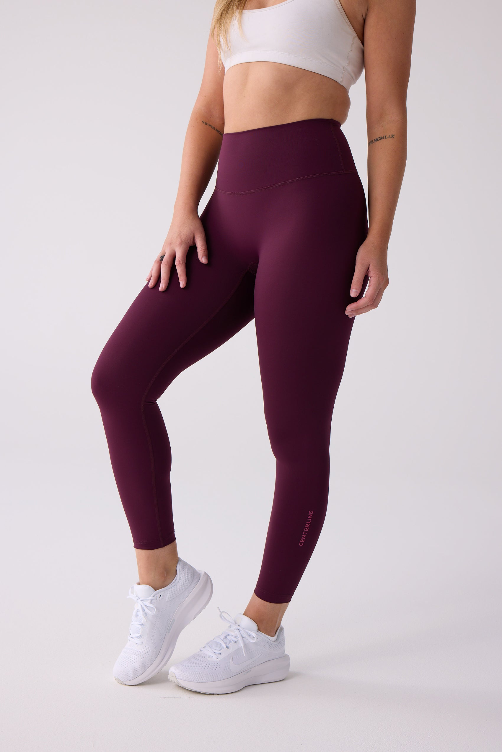 Maroon 7/8 leggings by Centerline Athletics, high-waisted, with 'CENTERLINE' text on the calf, worn with a white sports bra and white sneakers.