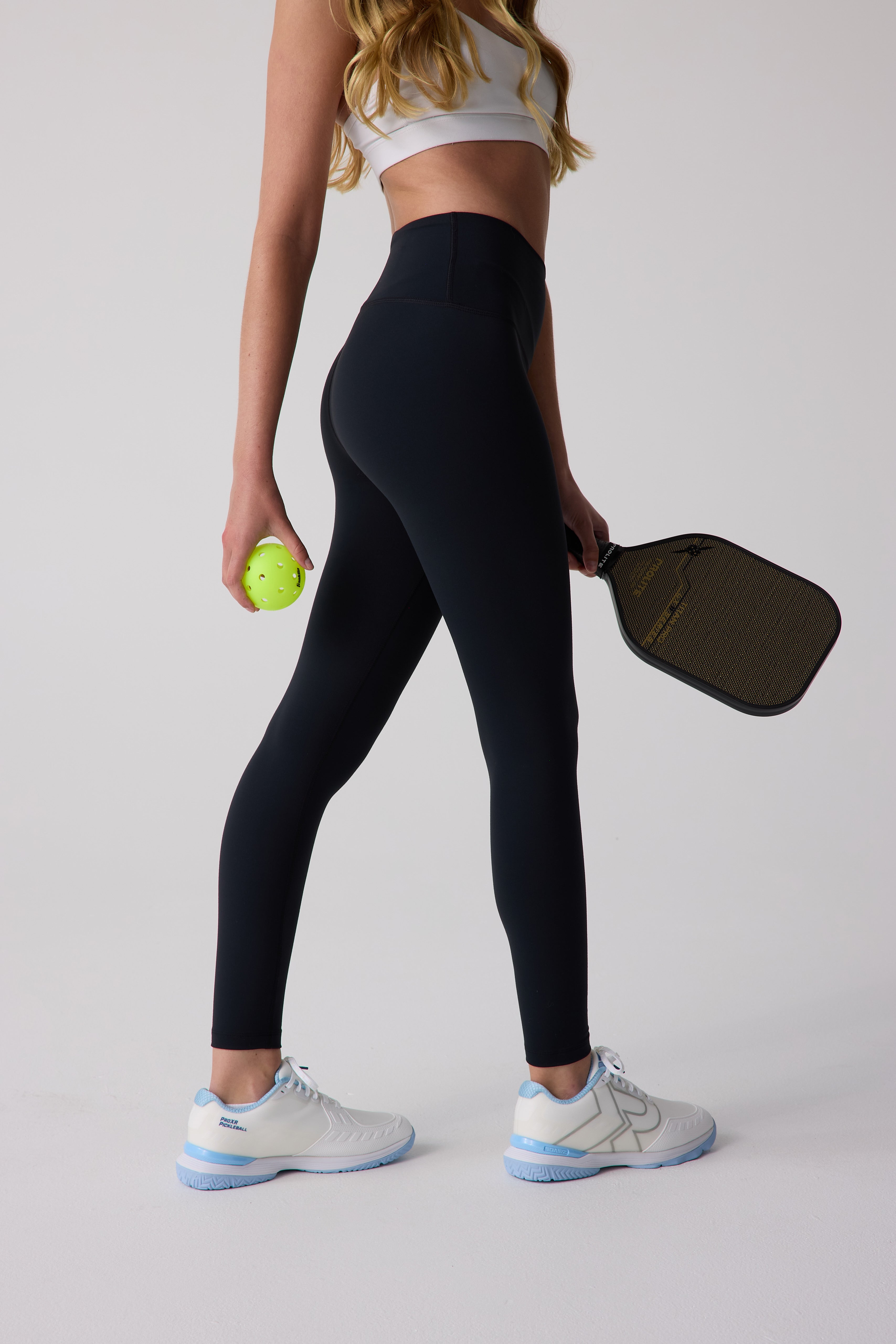 Black 7/8 length leggings by Centerline Athletics, worn with a white sports bra, holding a pickleball and paddle.