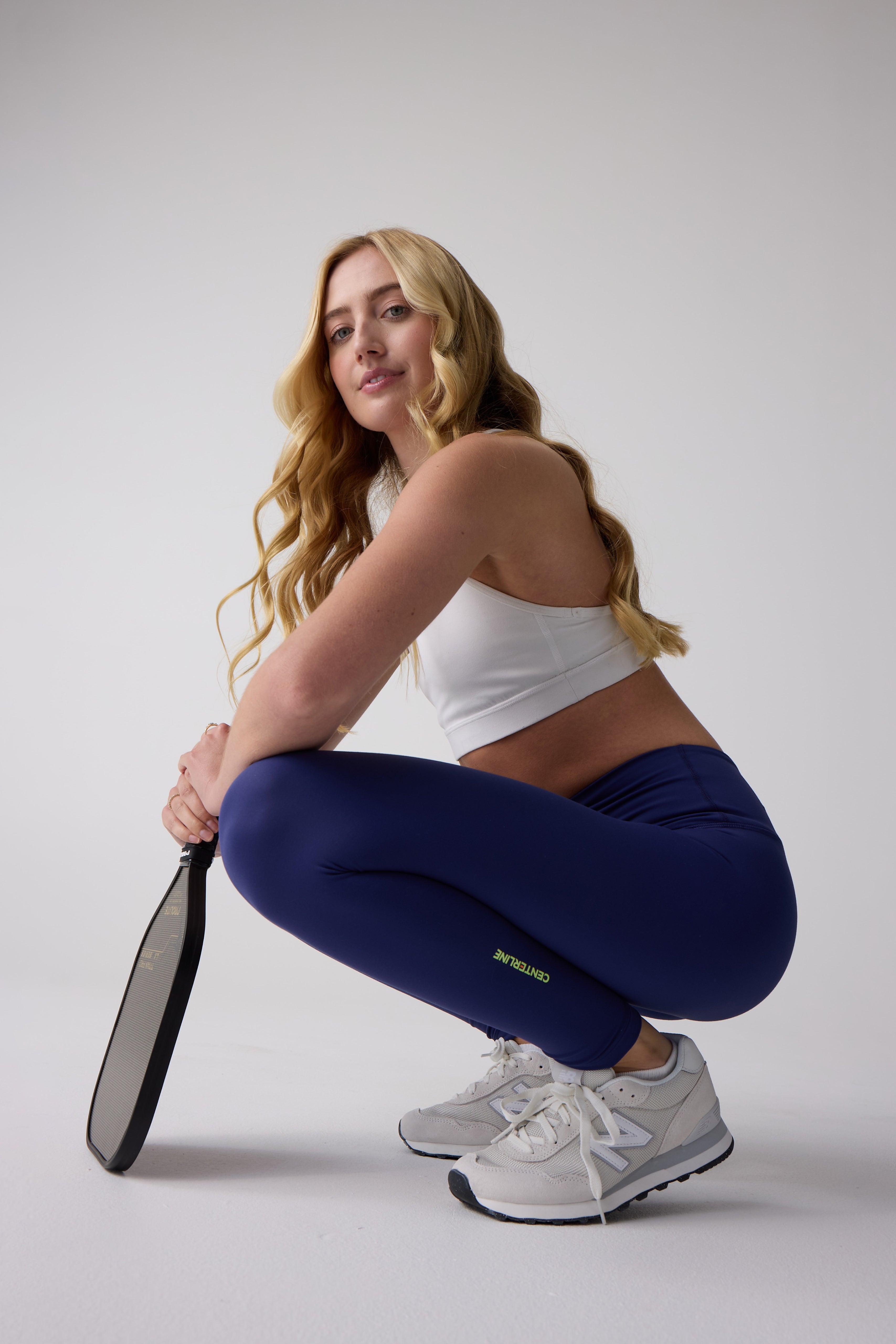 Dark blue 7/8 leggings by Centerline Athletics with green 'CENTERLINE' text on the calf, worn by a woman crouching.