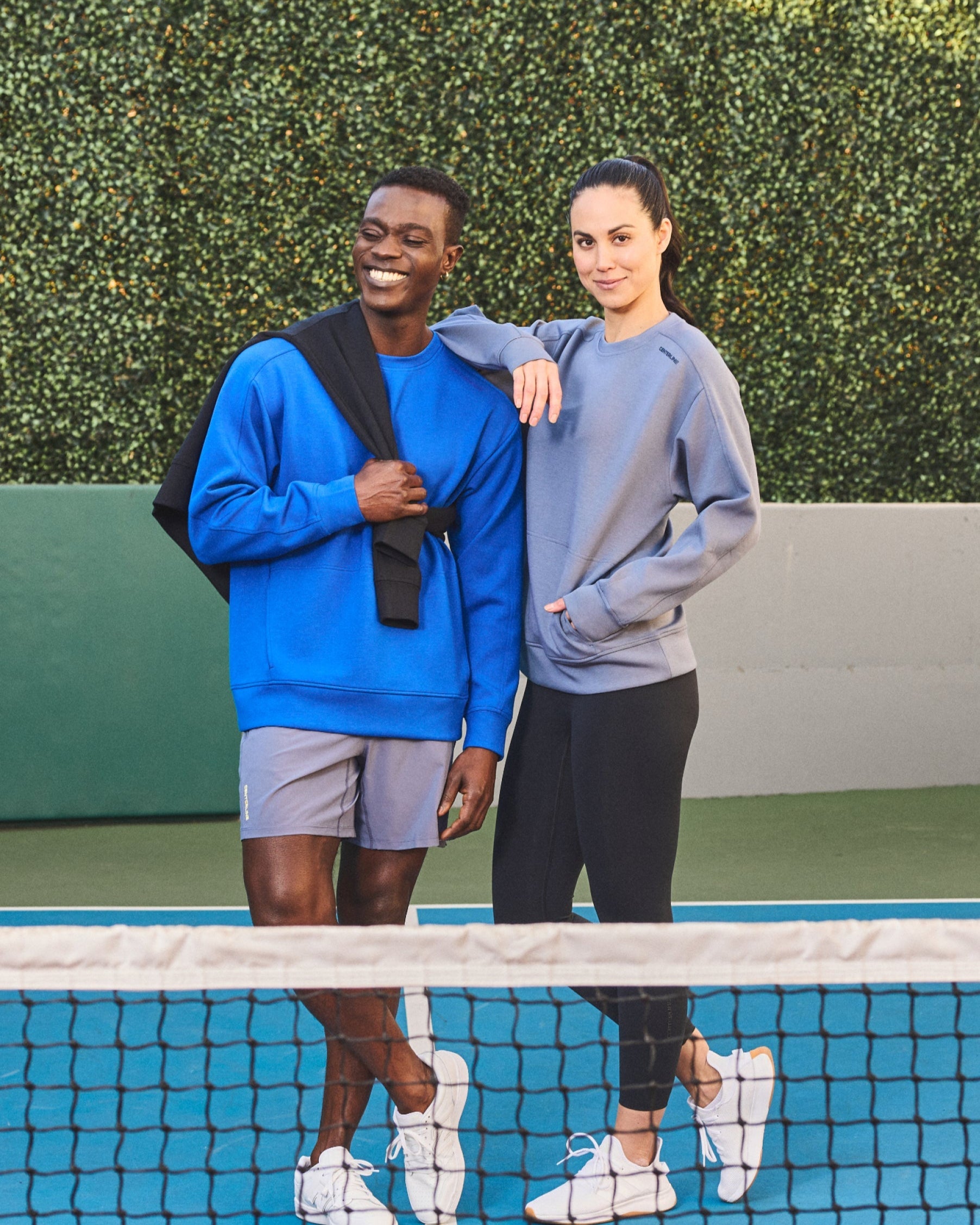 Two people wearing casual athletic clothes on a tennis court.