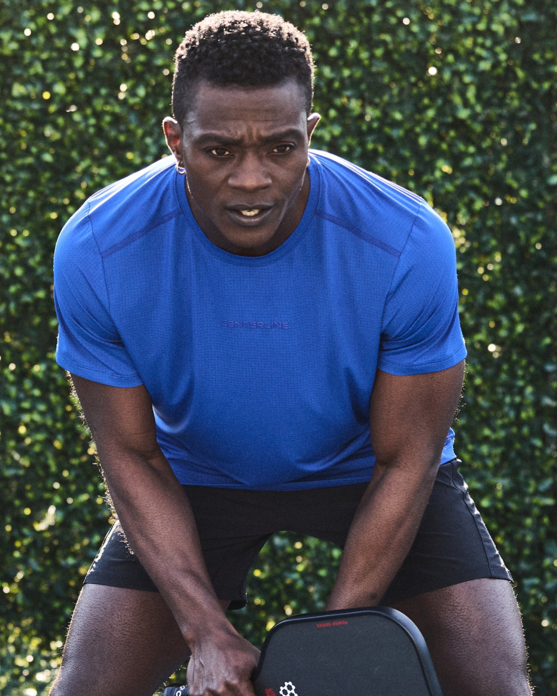 Man in blue workout shirt and black shorts holding workout equipment.