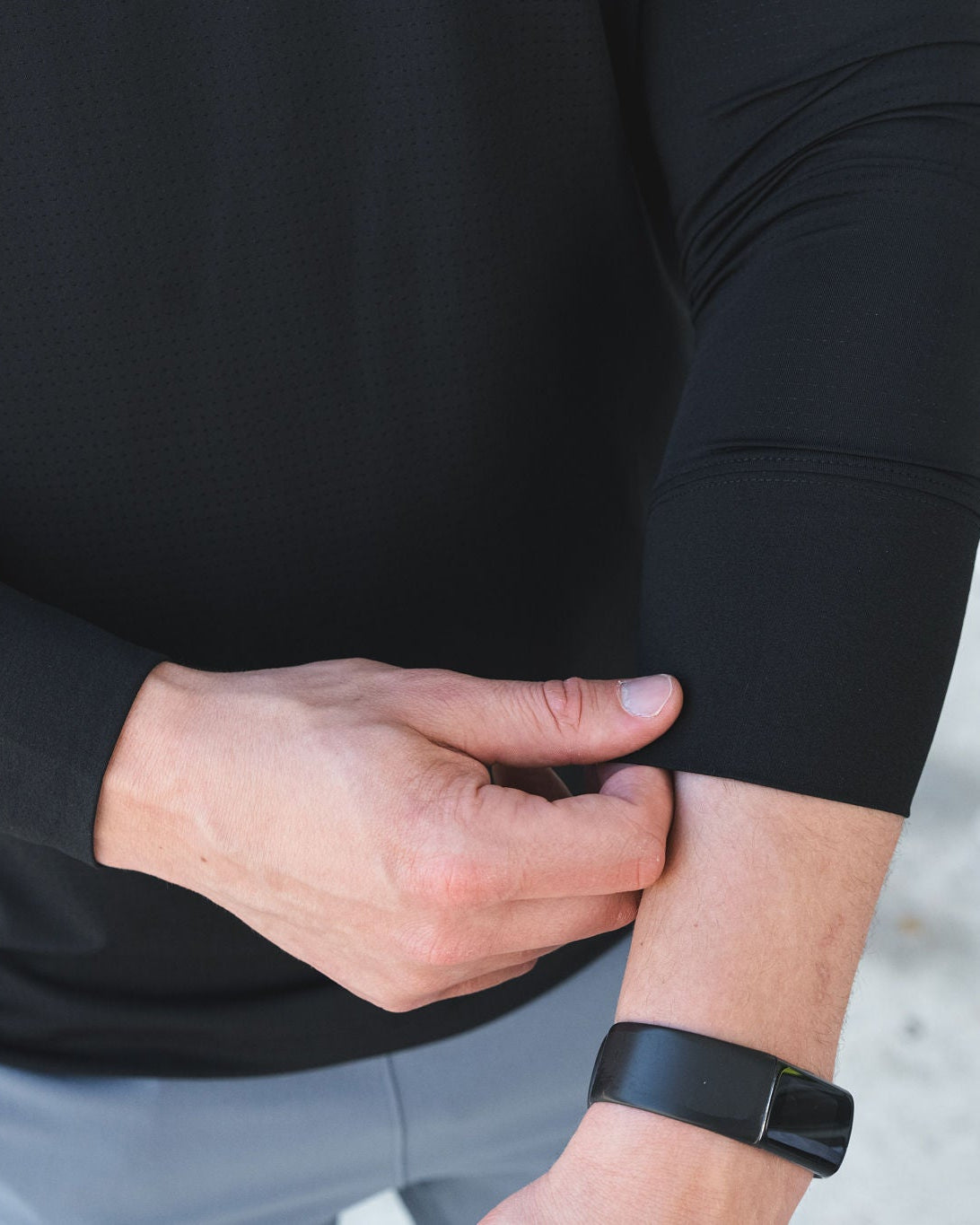 Man in black long-sleeve shirt with fitness tracker adjusting sleeve.
