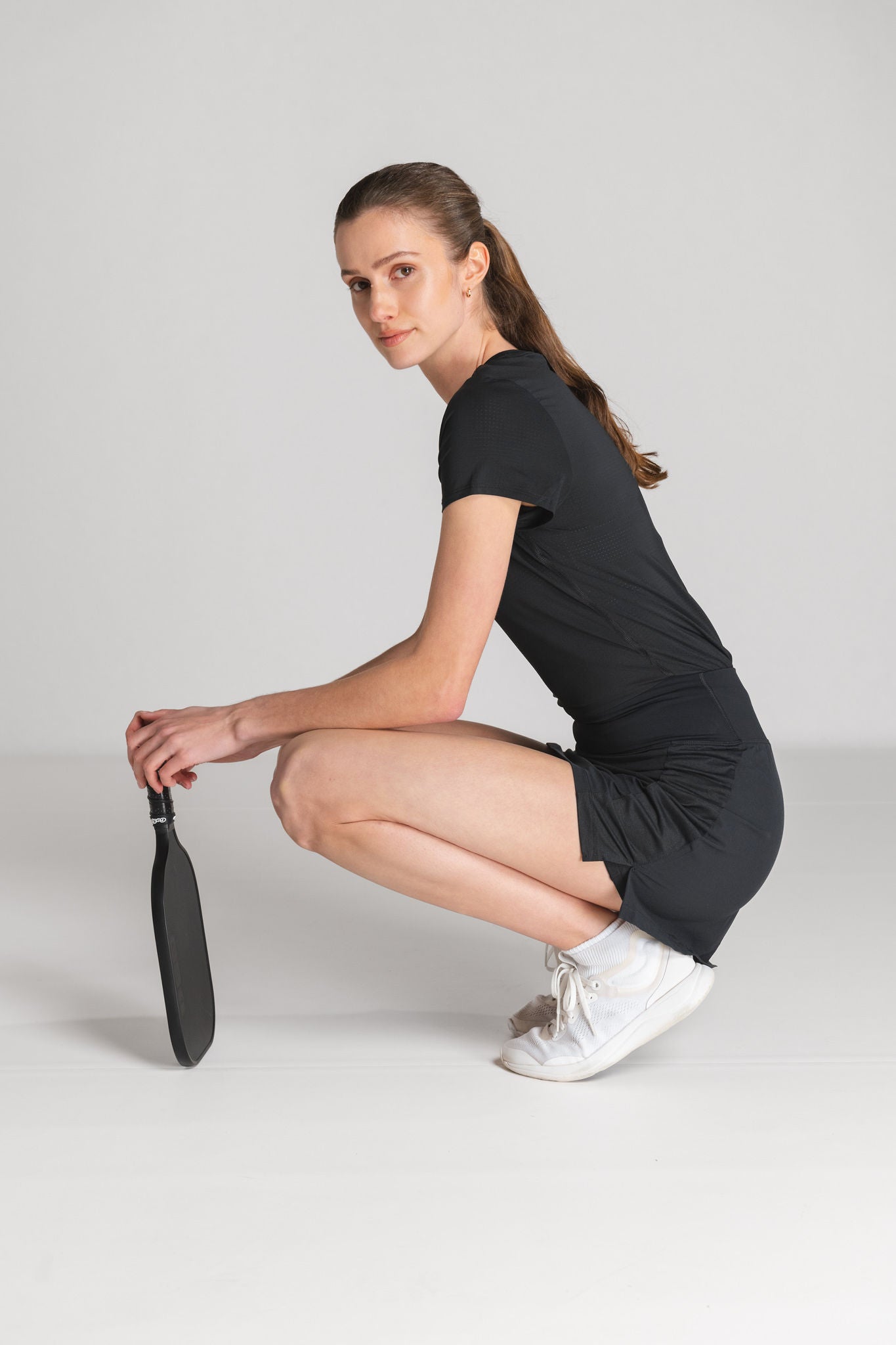 Woman in black sportswear crouching and holding a racquet.