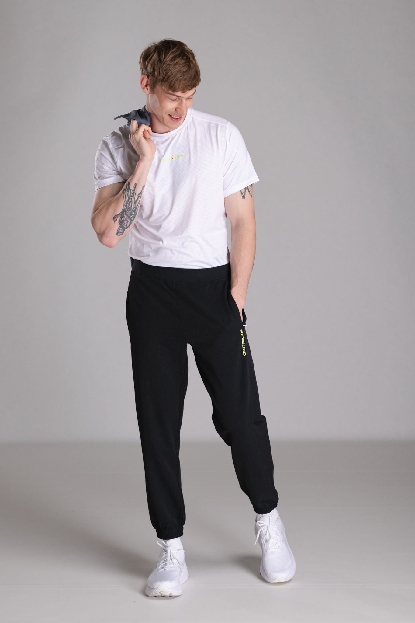 Man in white shirt and black joggers, standing indoors.