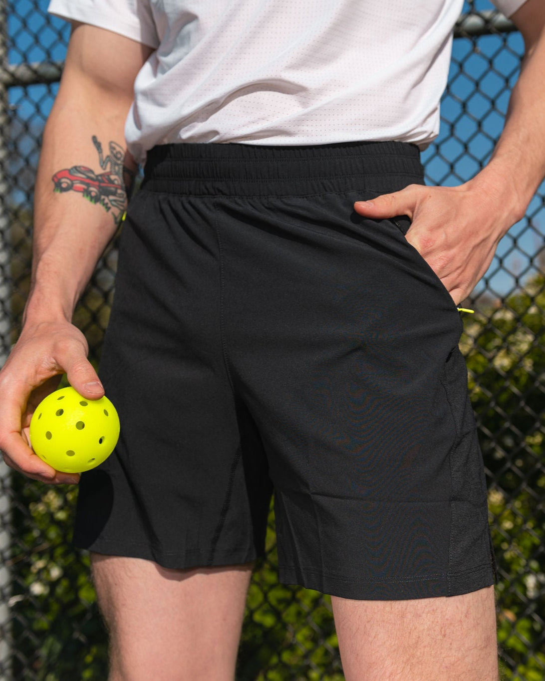 Man holding a yellow pickleball, wearing black athletic shorts and a white shirt.