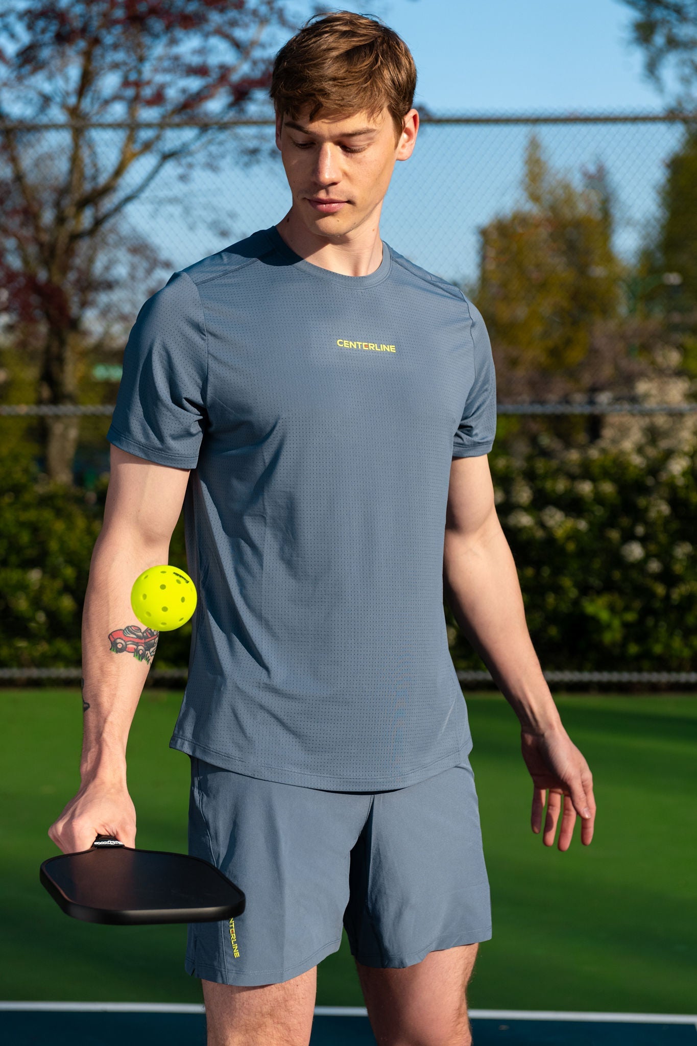 Man in grey athletic wear with pickleball paddle and ball on a court.