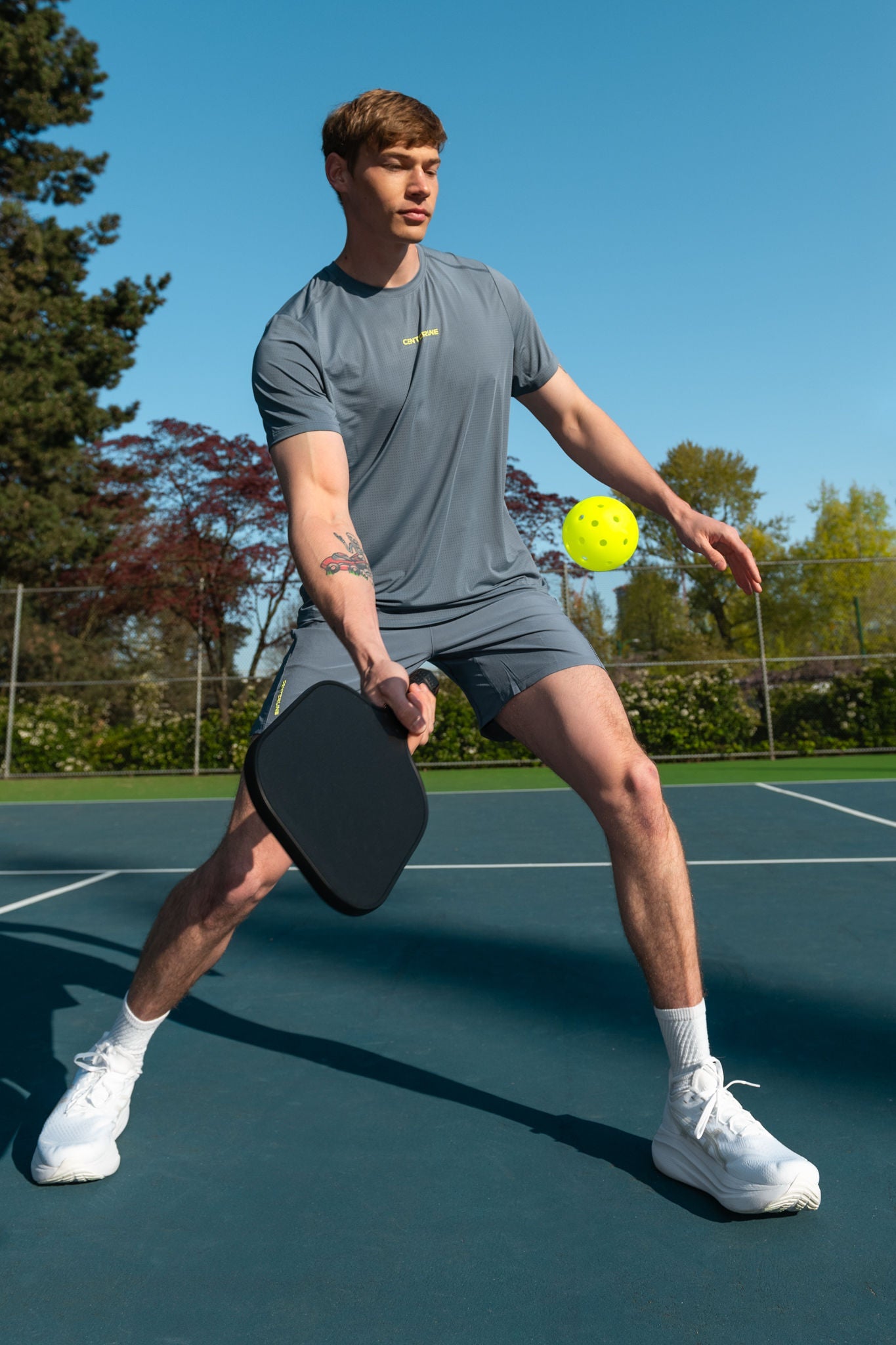 Man playing pickleball on a court in gray sportswear and white sneakers.