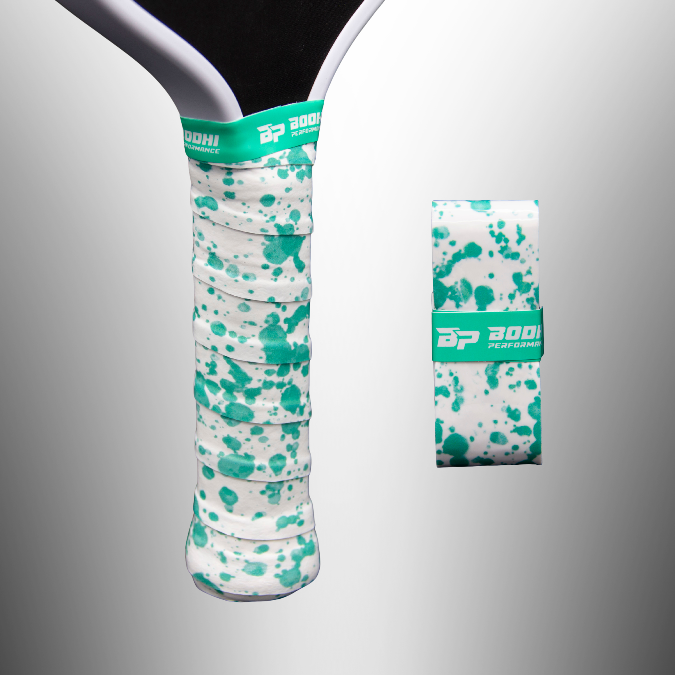 White performance paddle overgrip with green splatter pattern by Bodhi Performance, one wrapped on a paddle, another rolled, both with a green logo band.