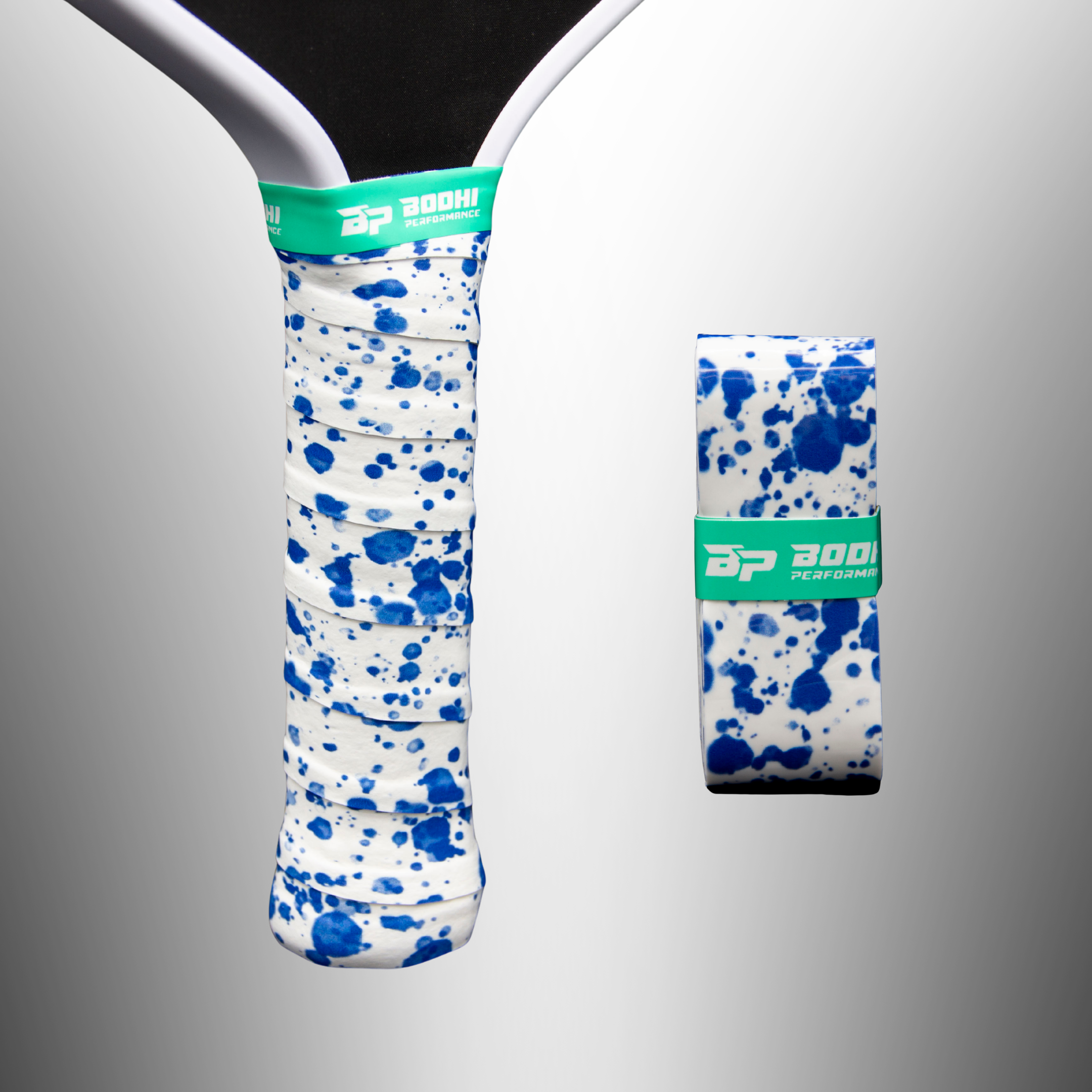 White overgrips with blue splatter pattern by Bodhi Performance, one on a paddle handle, one rolled with a green logo band.