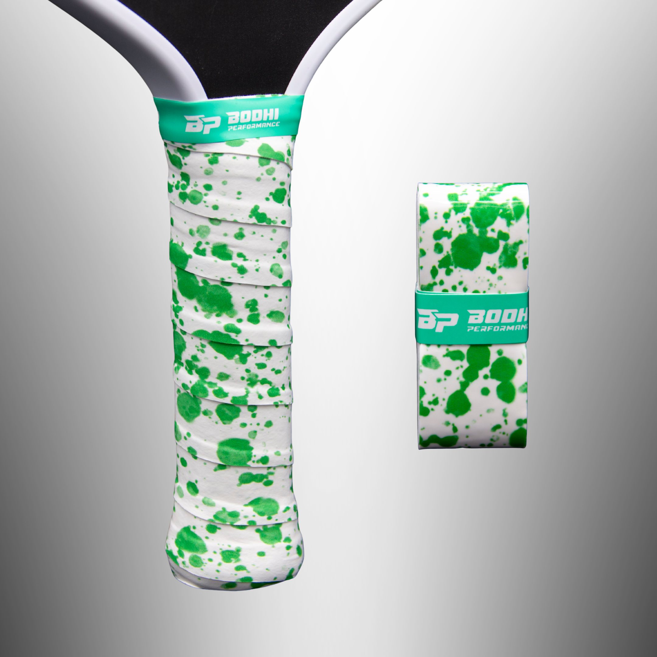 White overgrip with green splatter pattern by Bodhi Performance, wrapped on a paddle handle, with a rolled overgrip nearby.