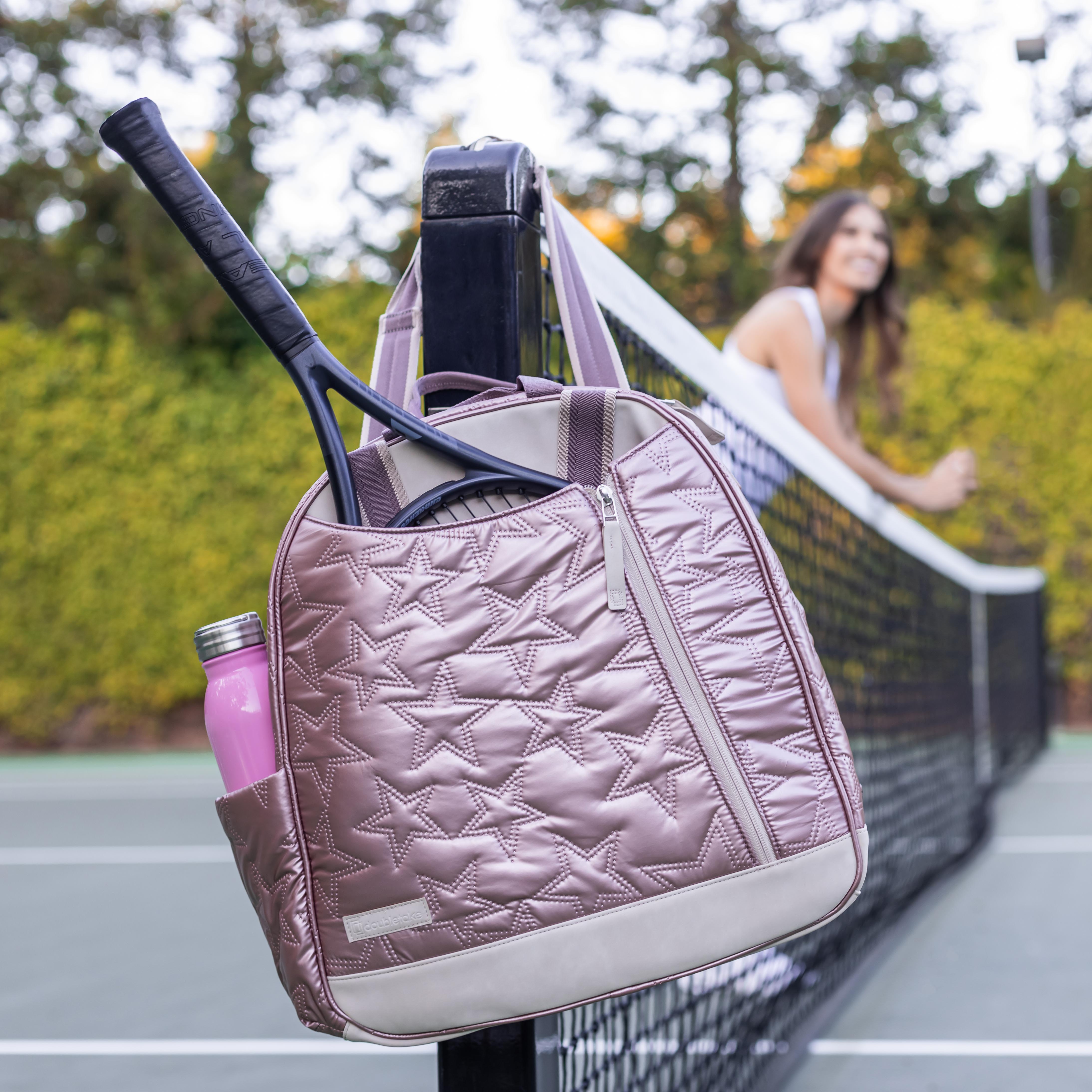 Shiny mauve quilted tennis backpack & tote by Doubletake with star patterns, holding a racket and water bottle, hanging on a net post.