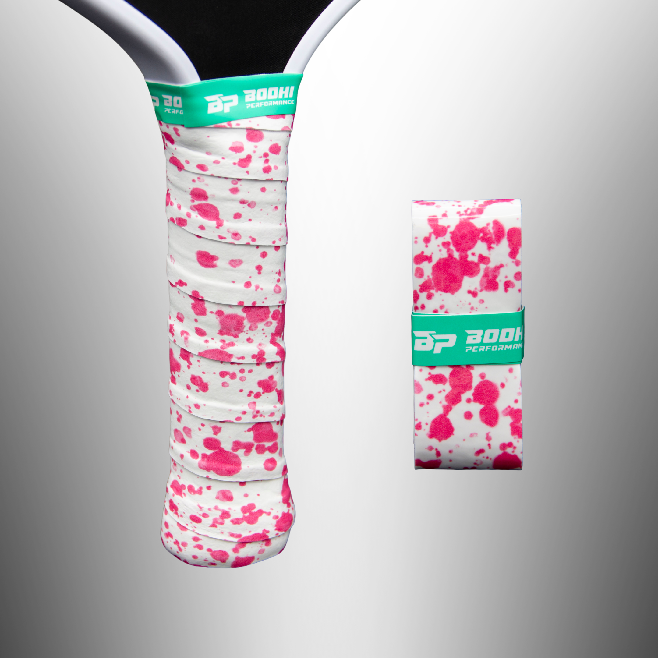 White overgrip with pink splatter pattern by Bodhi Performance, wrapped on a paddle handle and a separate rolled overgrip with a green band.