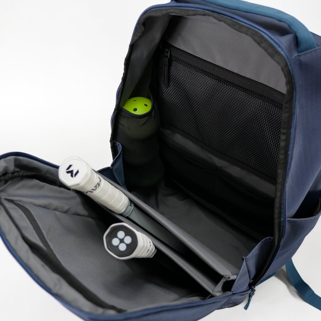 Navy blue pickleball backpack by FORWRD, open to reveal internal compartments, two paddles, and a yellow pickleball in a mesh pocket.