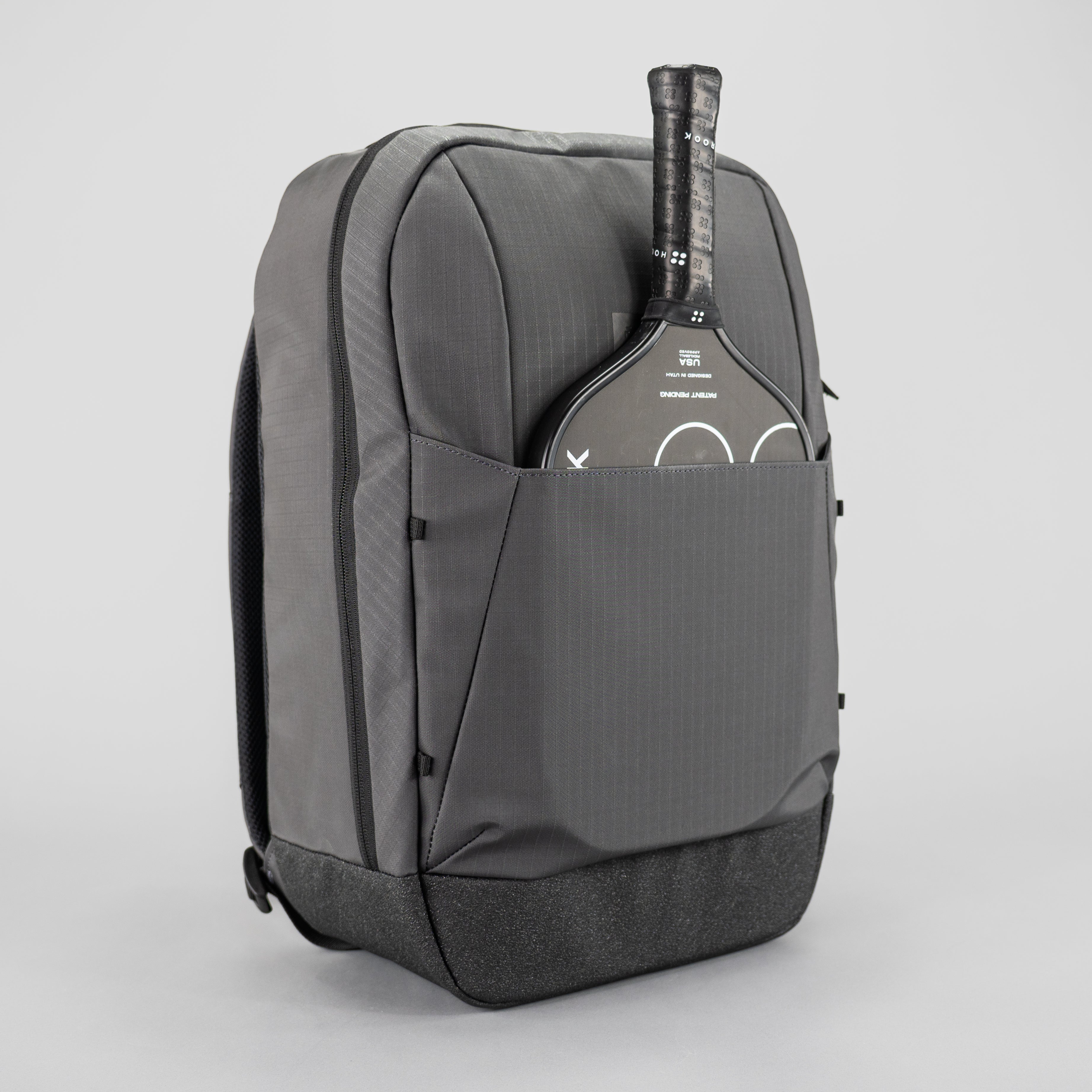 Dark grey pickleball backpack by FORWRD with subtle textured fabric, featuring a pickleball paddle in the front pocket and a granular textured base.