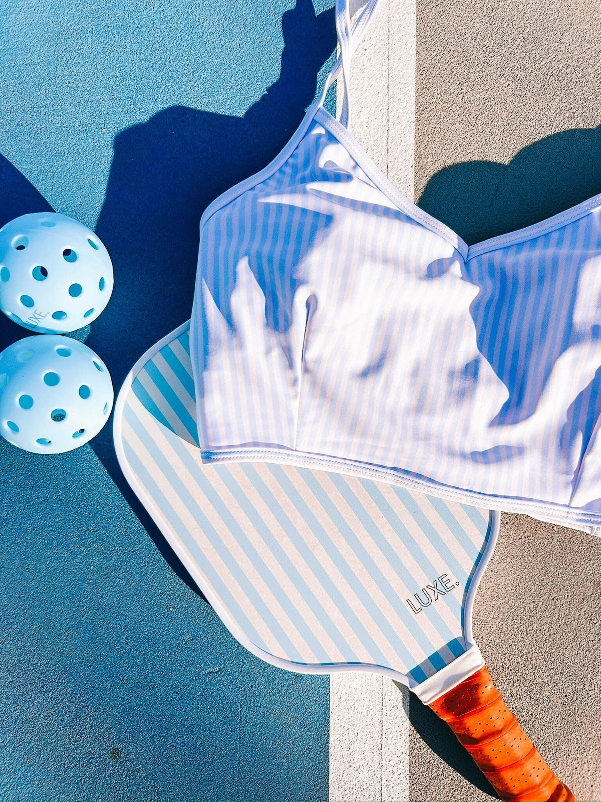 Pickleball paddle, bikini top, and balls on a blue and tan surface.