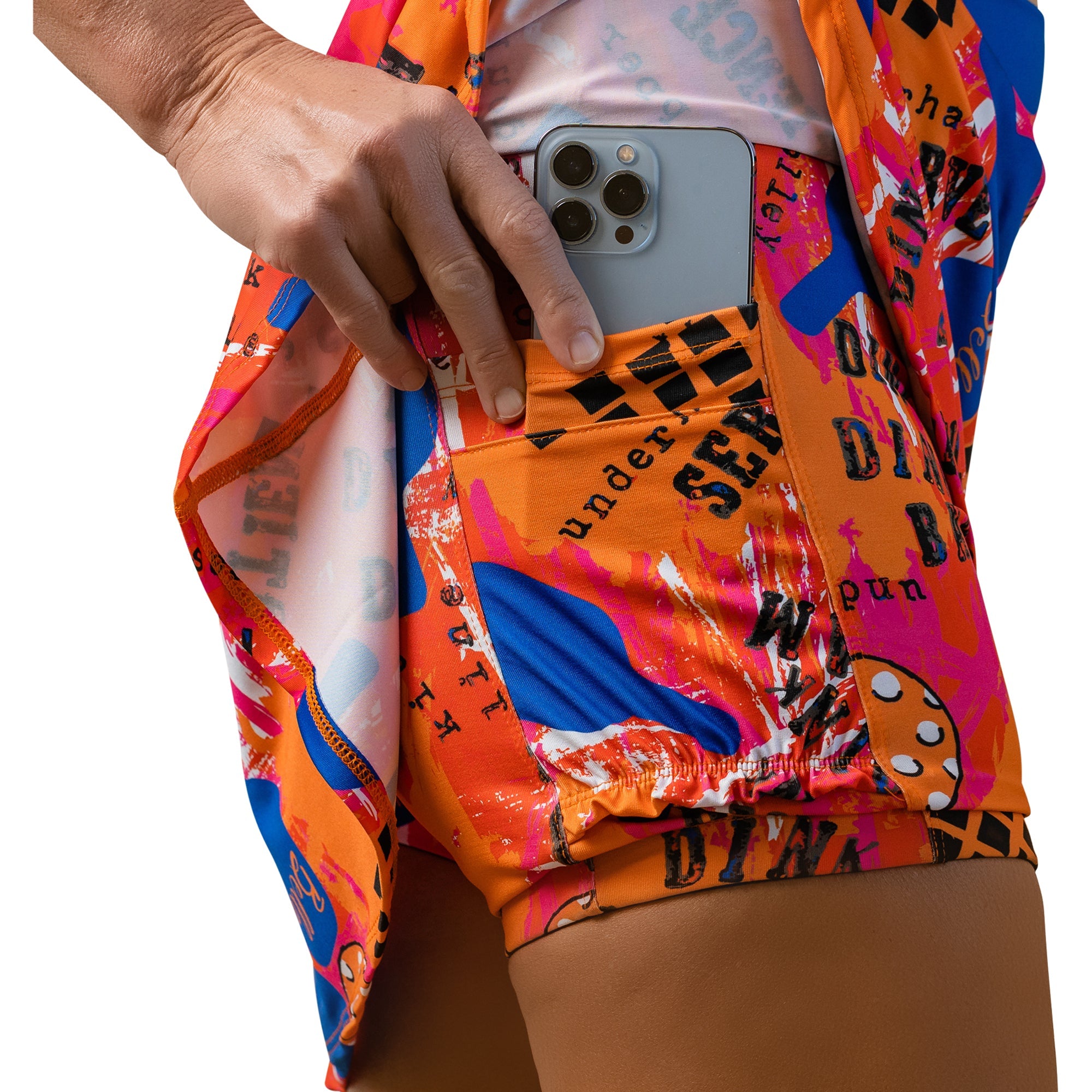 An A-line skort in a vibrant multi-color graffiti print by Pickleball Bella, with a hand placing a smartphone into a side pocket.