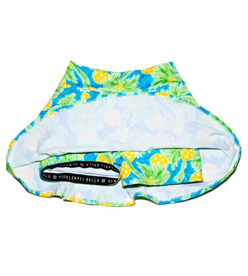 Blue A-line skort by Pickleball Bella with green palm leaves and yellow pickleball pattern, shown inside out revealing built-in shorts.