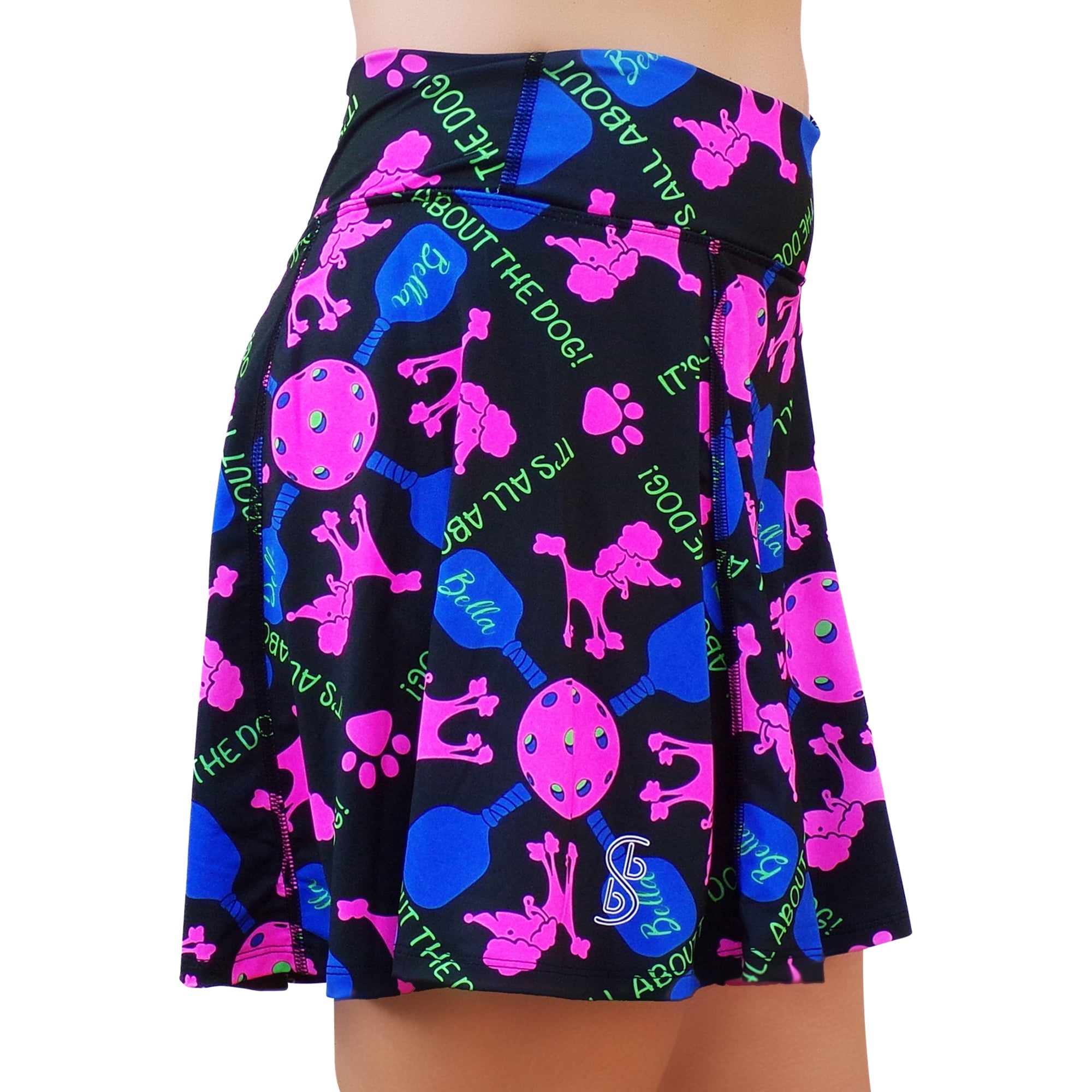 Black patterned A-line skort by Pickleball Bella, featuring pink poodles, blue pickleball paddles, green "IT'S ALL ABOUT THE DOG!" text, and pink paw prints, side view.