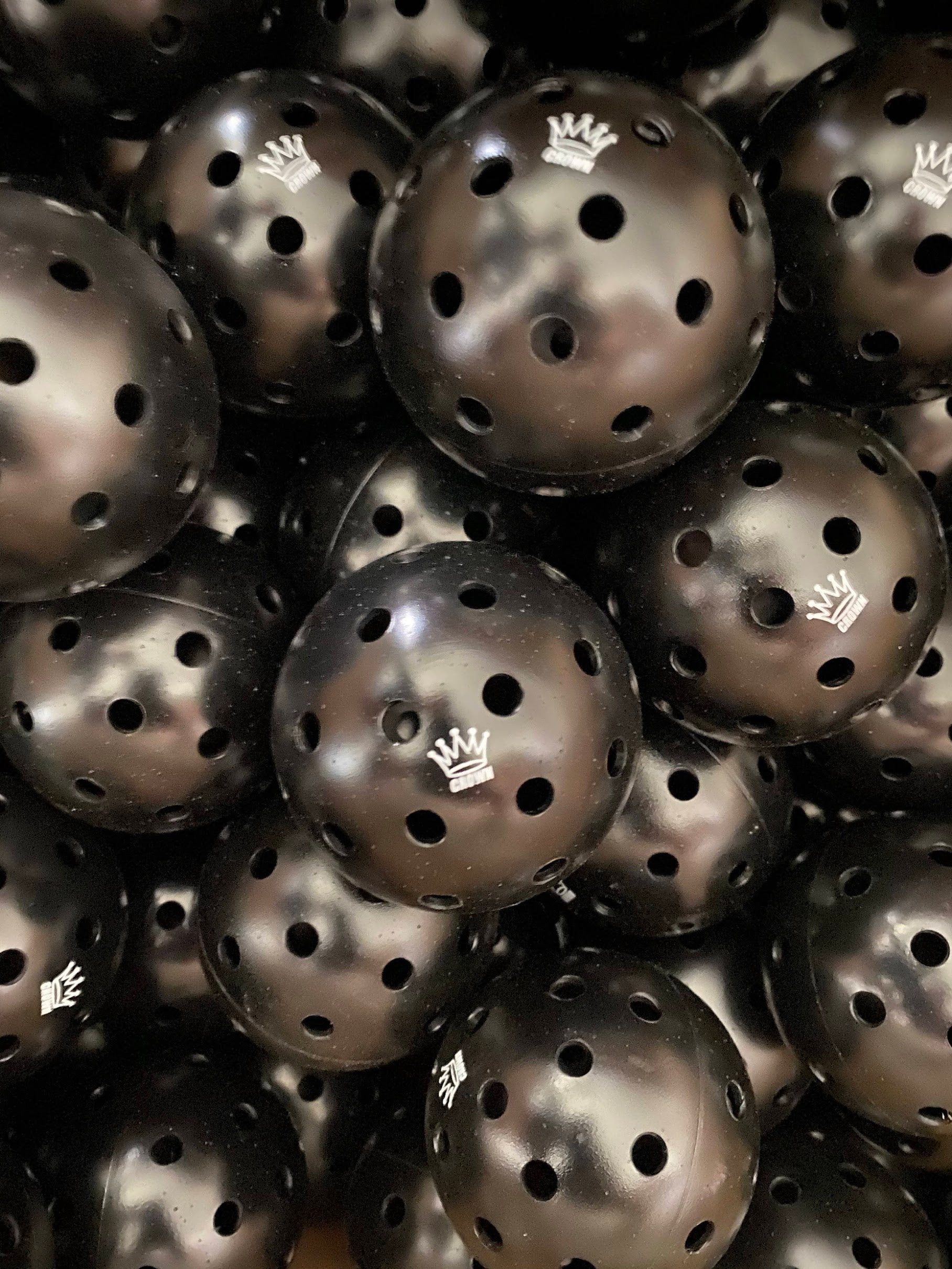 Pile of black plastic Wiffle balls with the "Crown" logo.