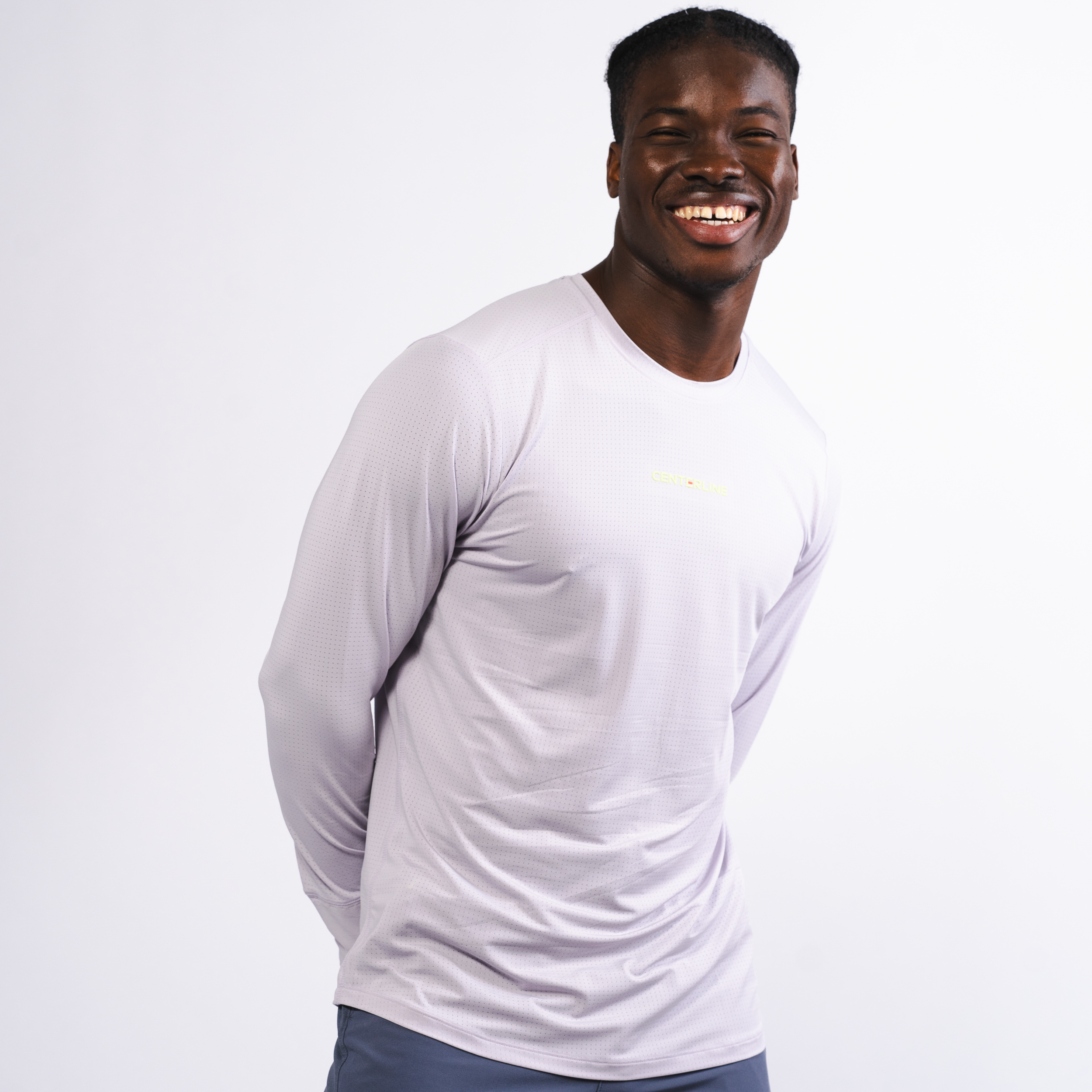 Smiling man in a lavender long-sleeve athletic shirt with a small logo and blue pants.