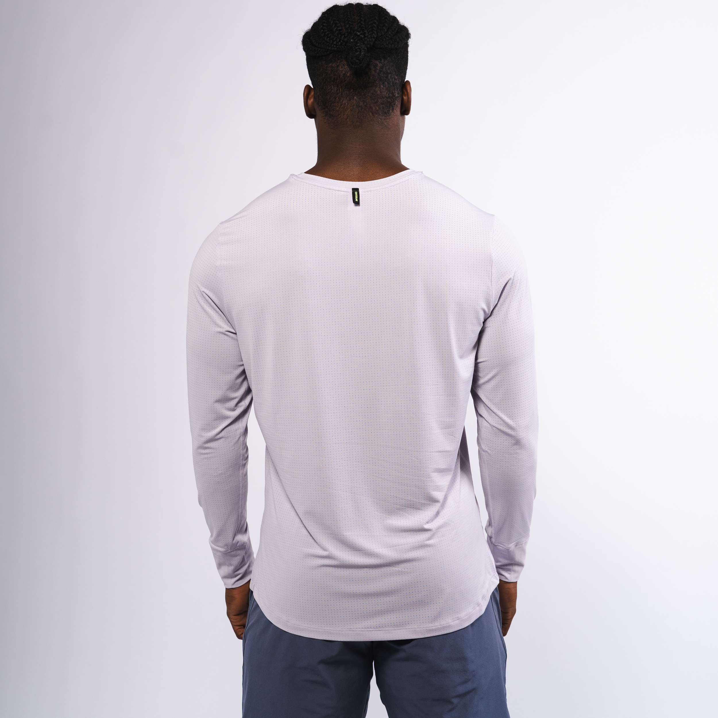 Man with braids wearing a gray long-sleeve shirt and blue shorts standing against a white background.