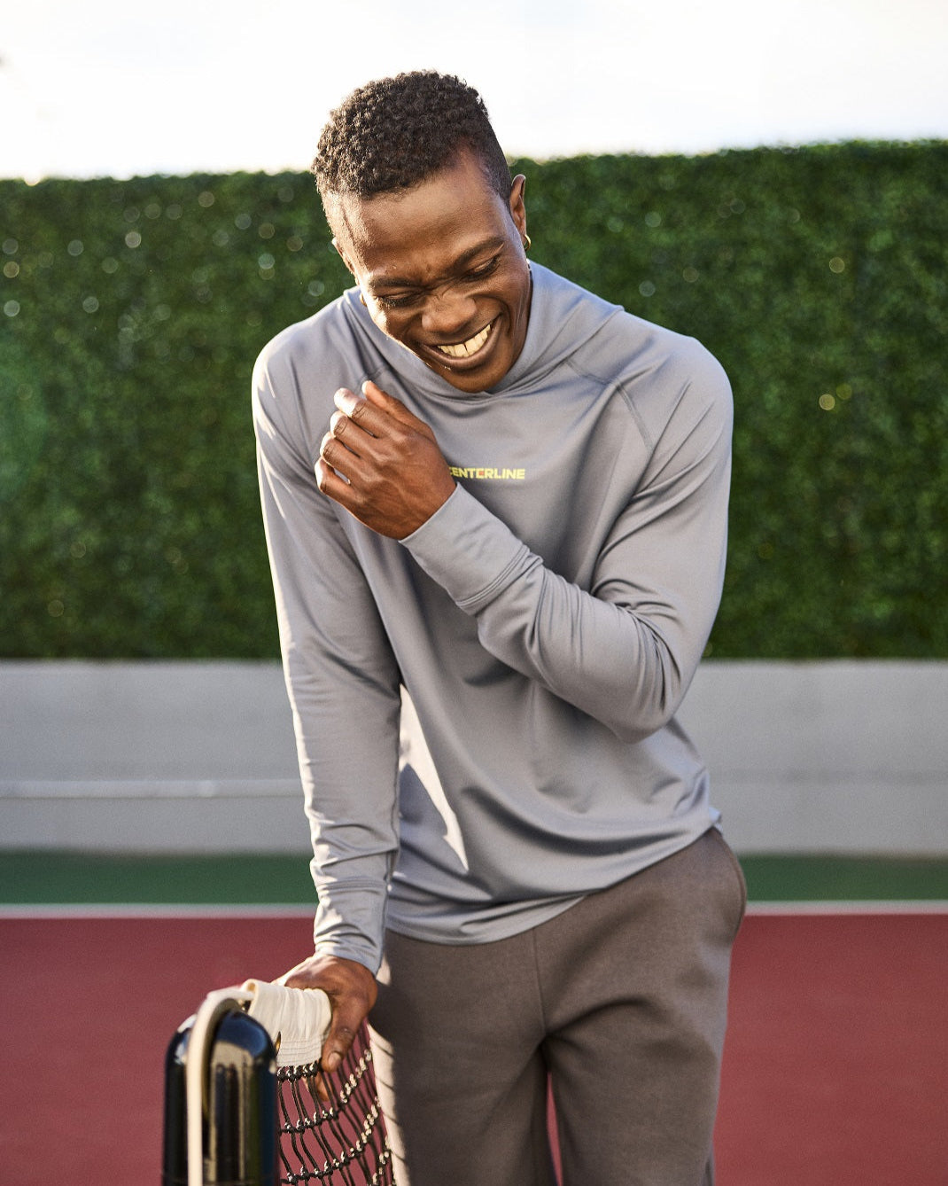 Man in gray athletic wear laughing on a tennis court.