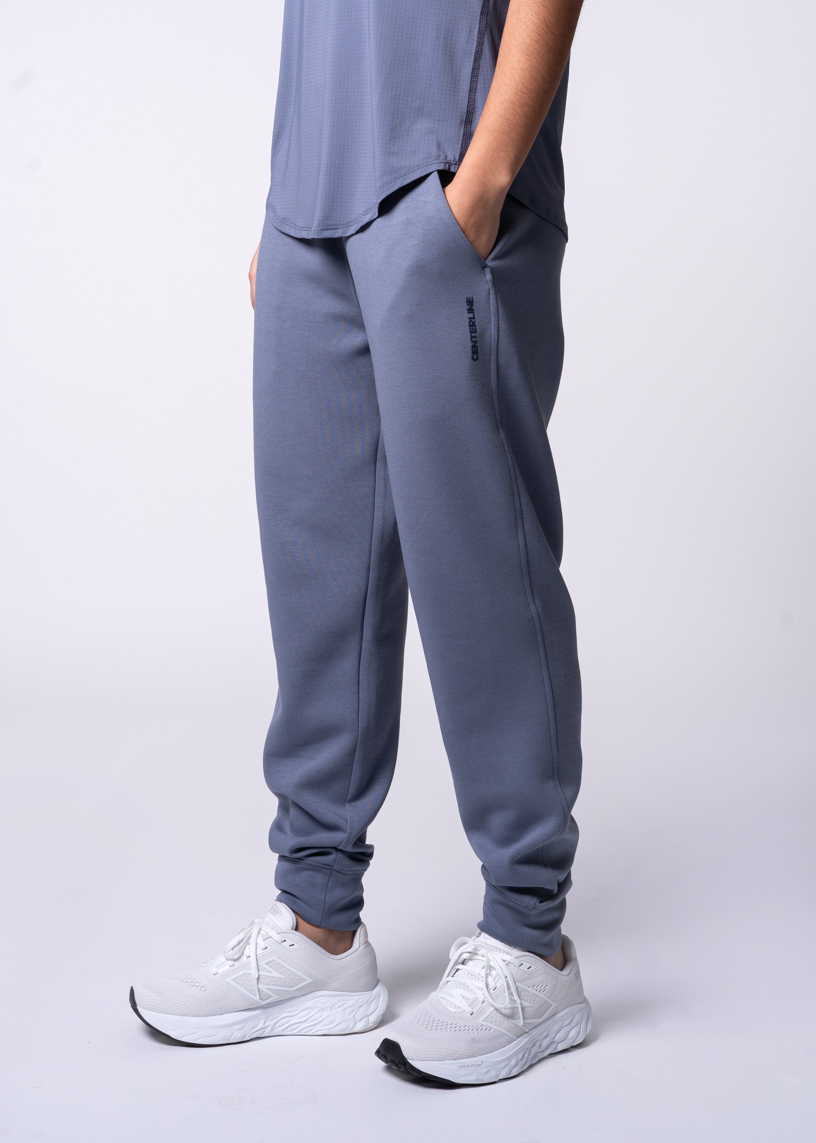 Person in gray athletic top and matching joggers with hand in pocket, wearing white sneakers.