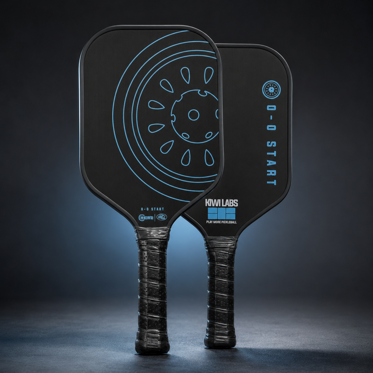 Two black raw carbon pickleball paddles from Kiwi Labs, featuring blue circular and vertical "0-0 START" designs, and textured black grips.