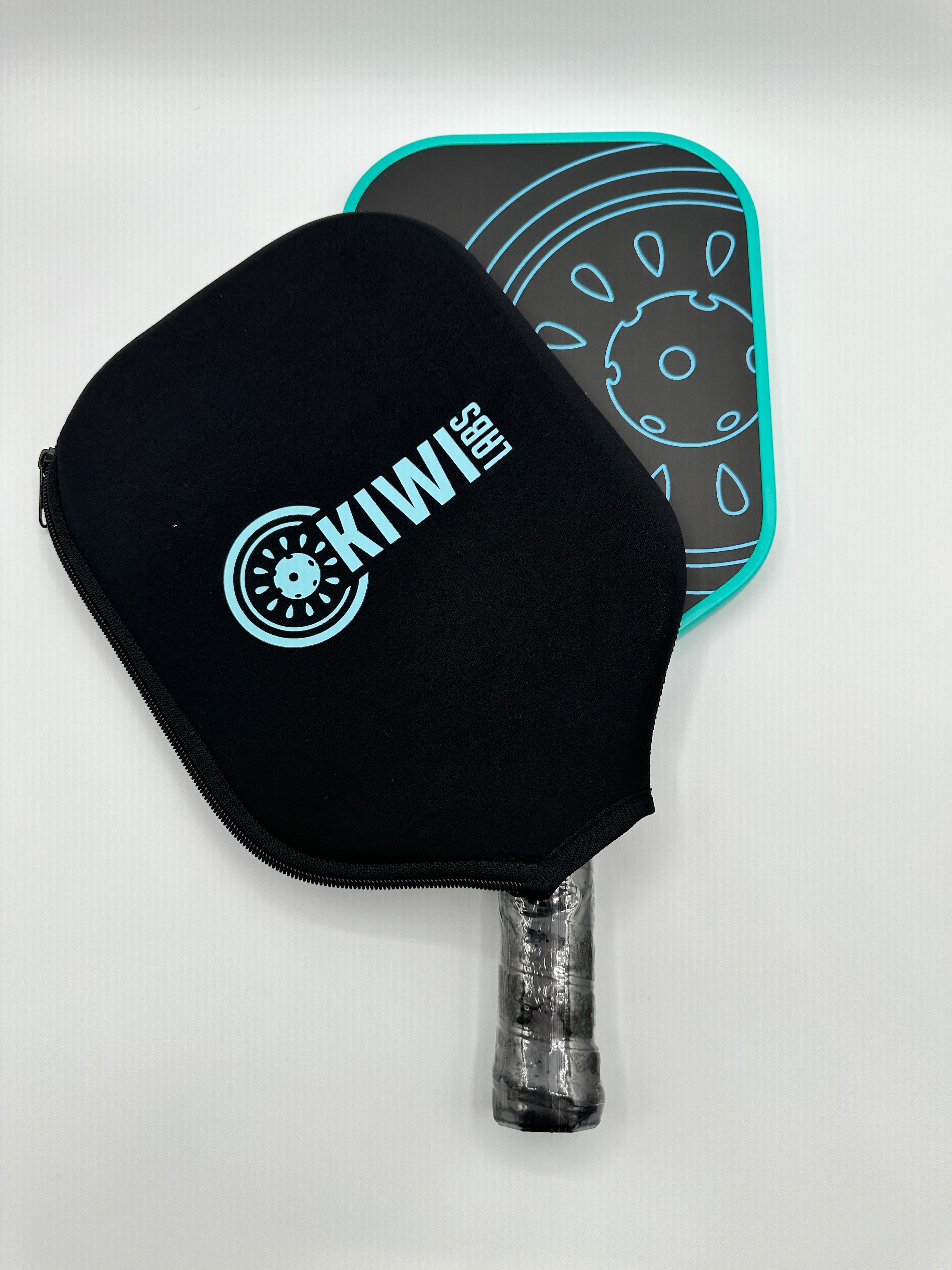 A pickleball paddle with a black cover that says "KIWI LABS" in teal is next to a black paddle with a teal design on a white background.