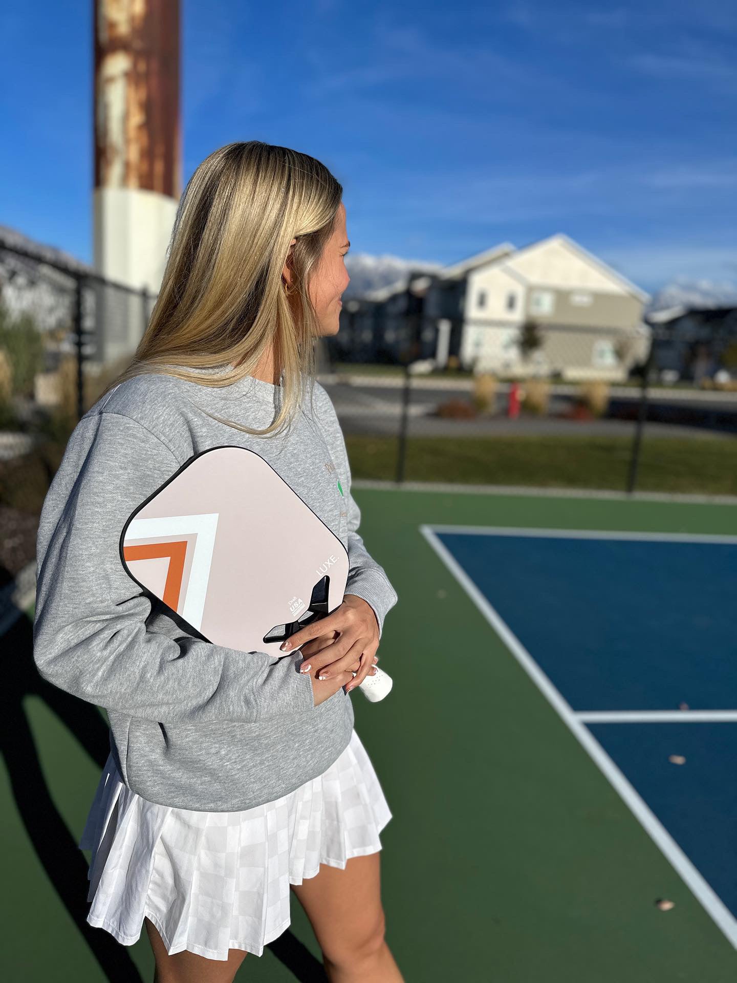 Grey pickleball sweatshirt from LUXE Pickleball, worn by a woman holding a paddle on a court.
