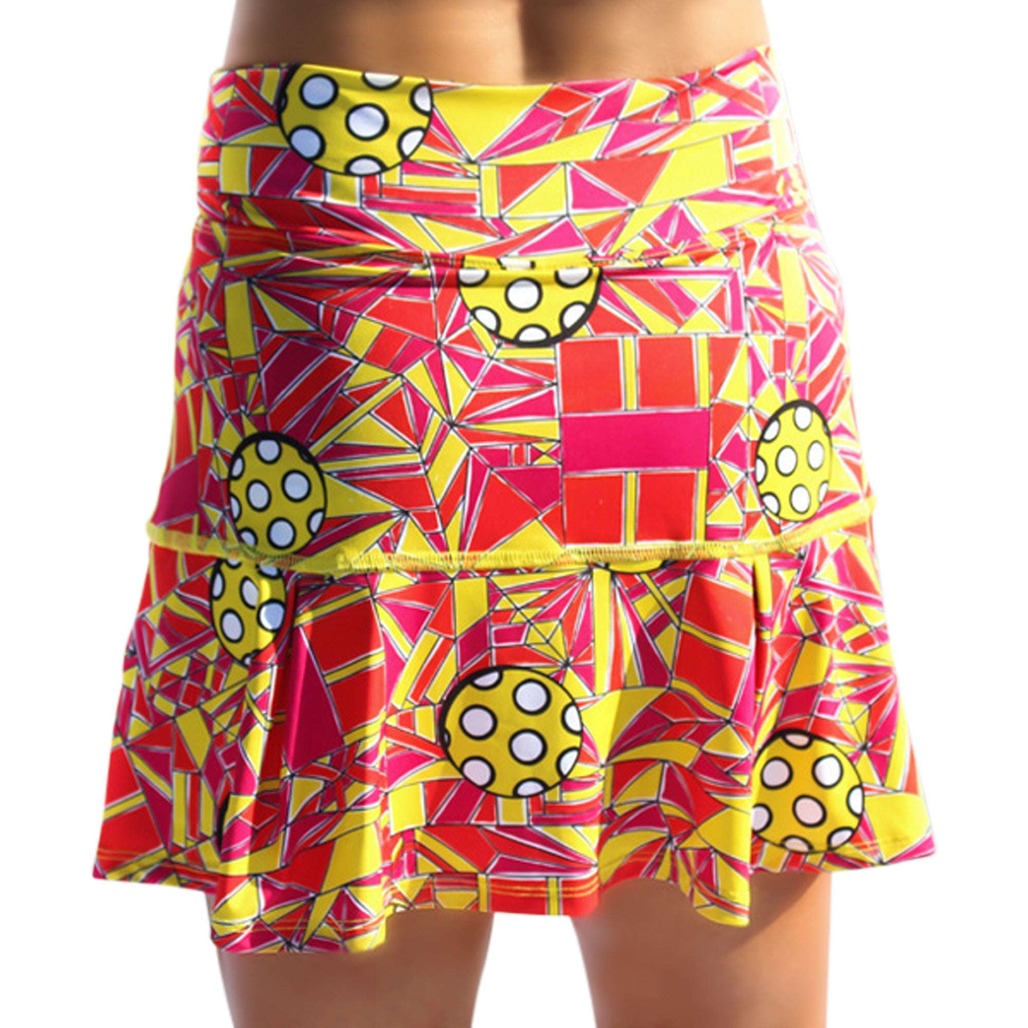 Colorful pleated skort by Pickleball Bella, featuring a geometric yellow, red, and pink pattern with pickleball designs and a drop pleat.