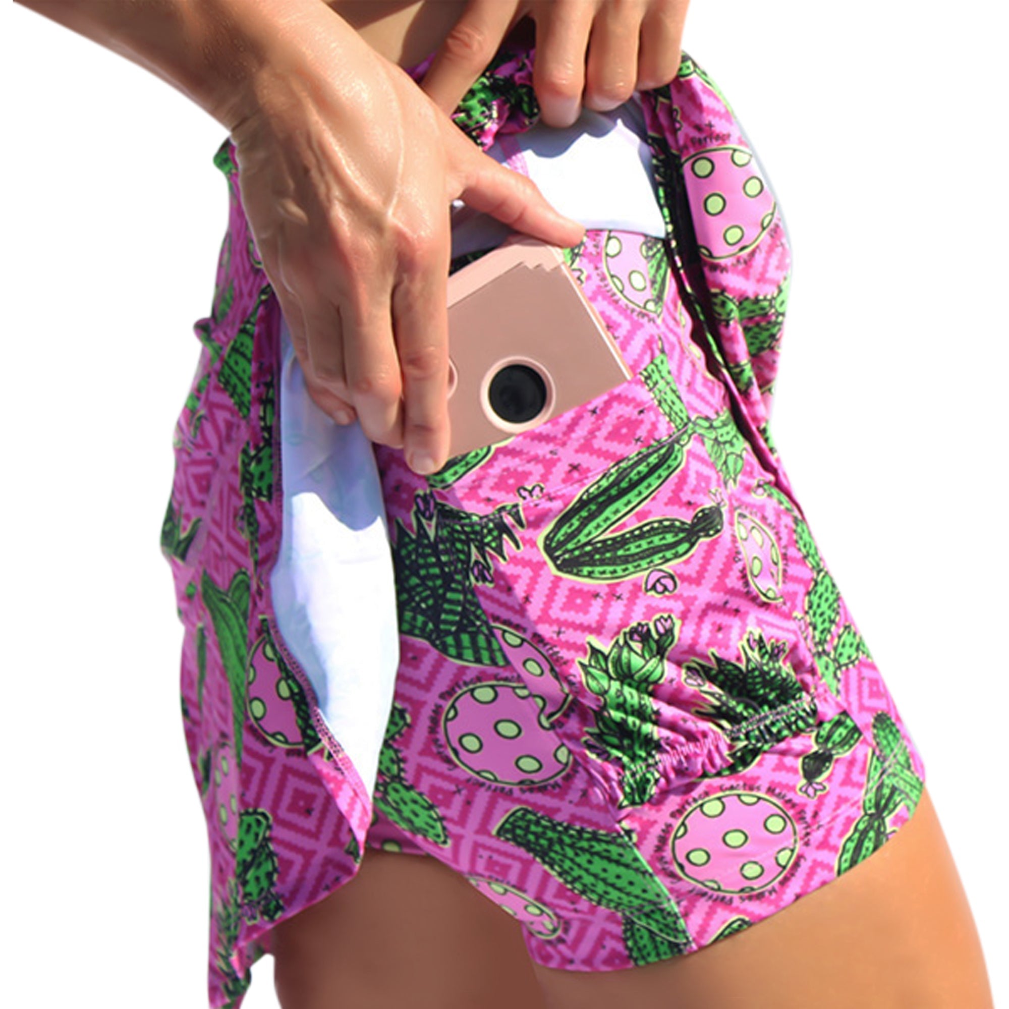 Pink and green pleated skort by Pickleball Bella, featuring a vibrant cactus pattern with a hand inserting a phone into its side pocket.