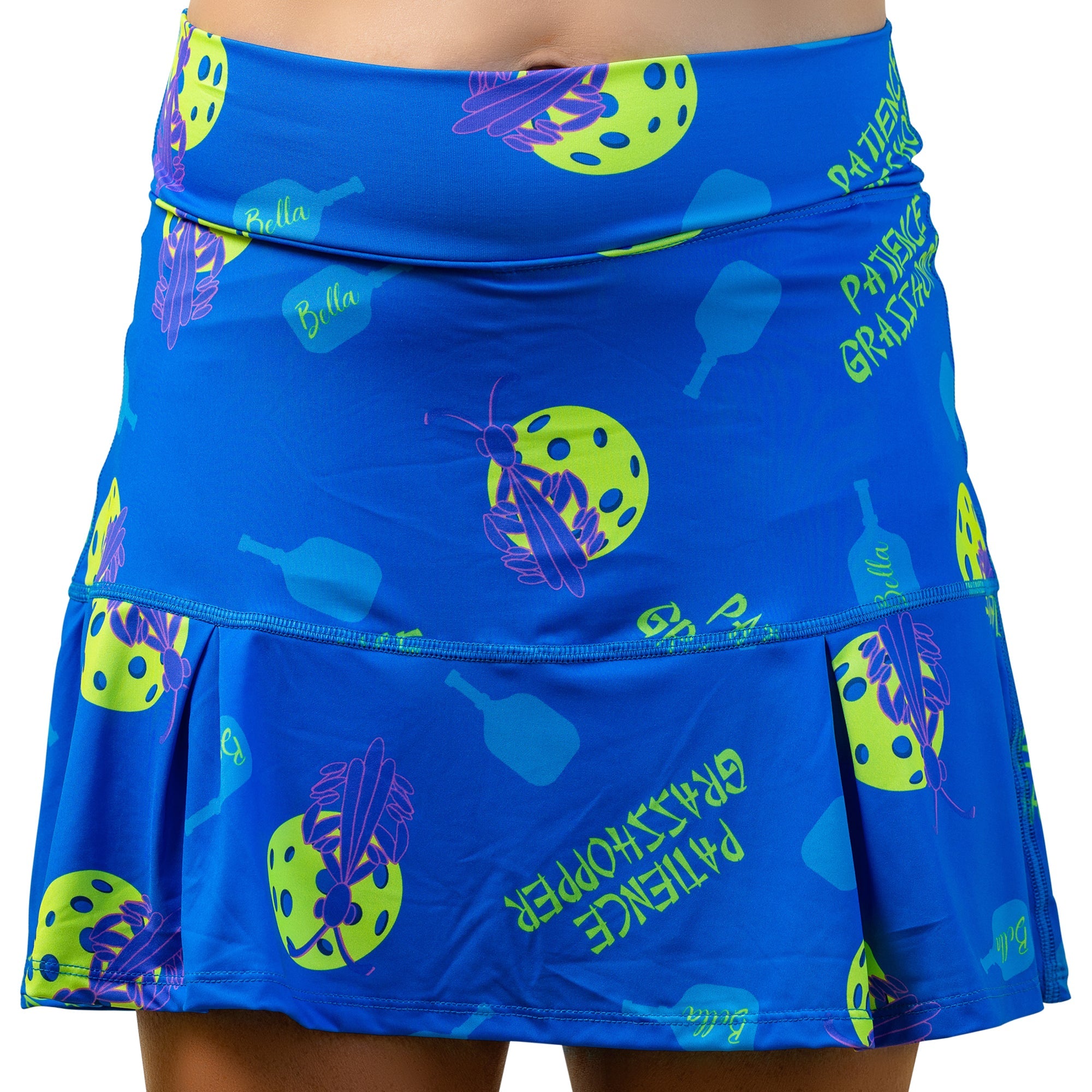 Blue drop pleat skort by Pickleball Bella featuring neon green pickleball, purple grasshopper graphics, "Patience Grasshopper" and "Bella" text.