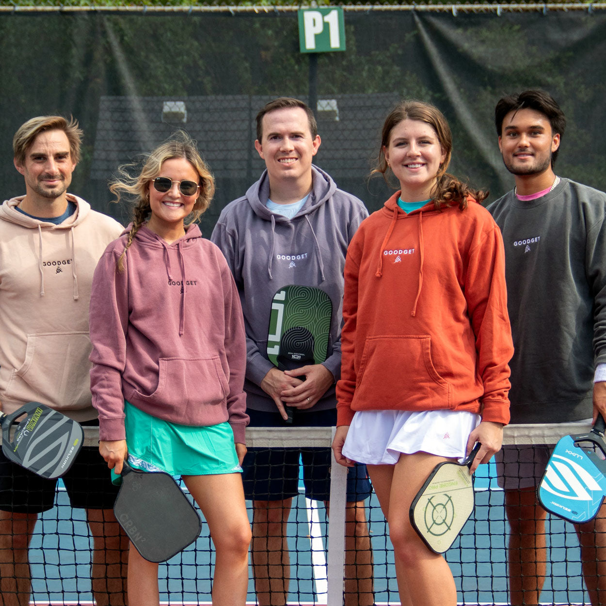 Men's Everyday Hoodie in various solid colors by Good Get, worn by diverse individuals on a pickleball court.
