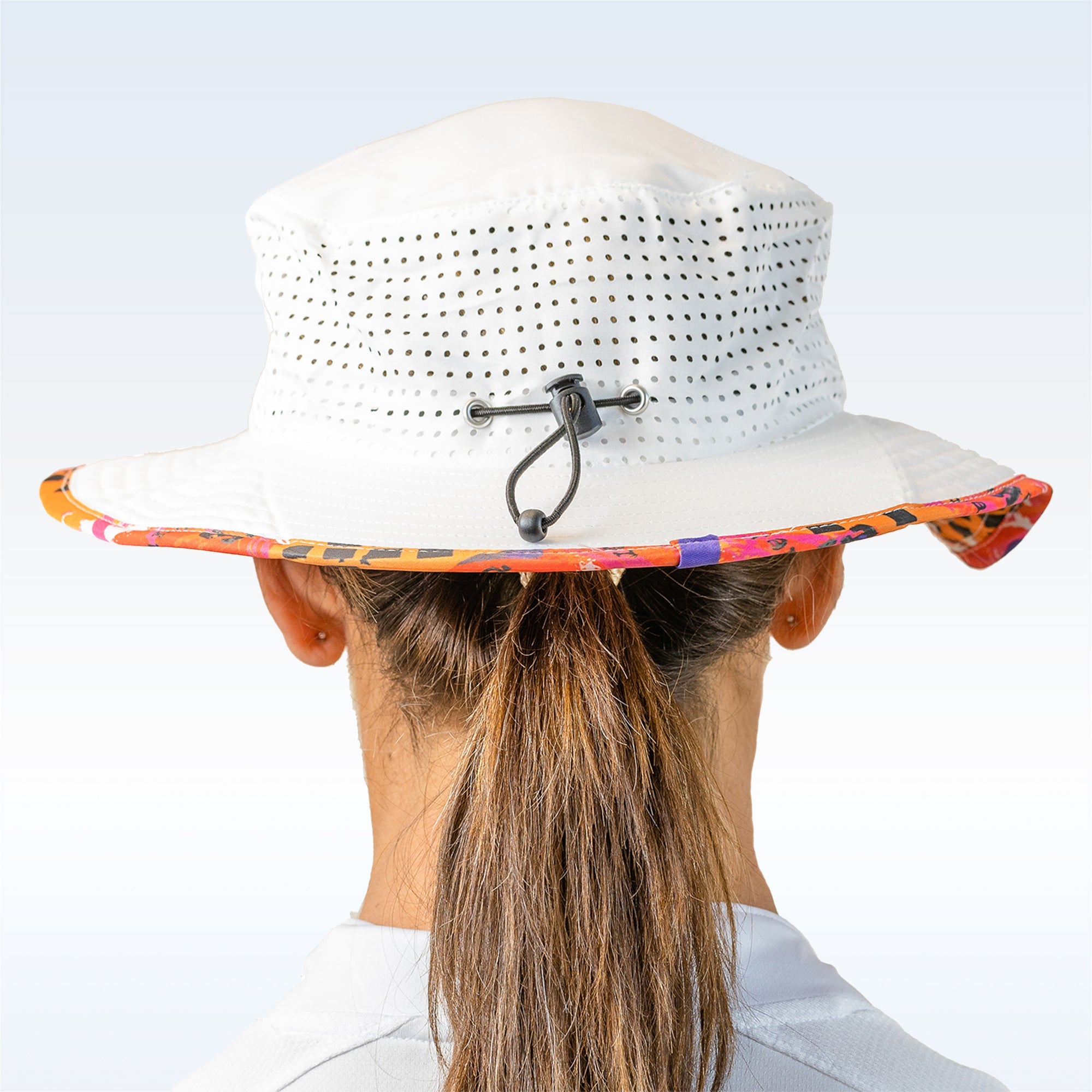 White perforated bucket hat by Pickleball Bella with a colorful patterned brim and adjustable drawstring worn over a ponytail.