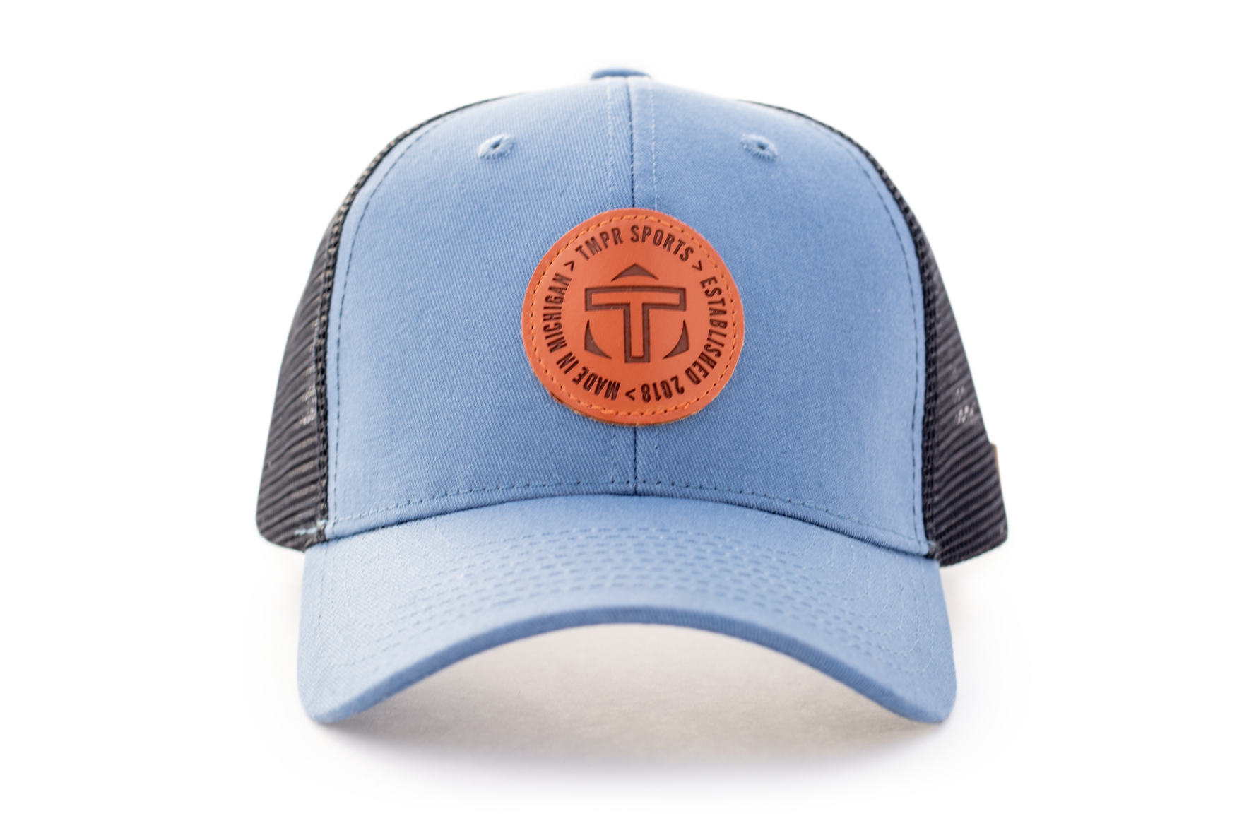 Light blue trucker cap by TMPR Sports with a dark mesh back and a round, brown embossed logo patch on the front.