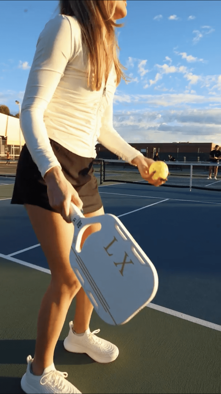 A woman playing pickleball with a white paddle and a yellow ball.
