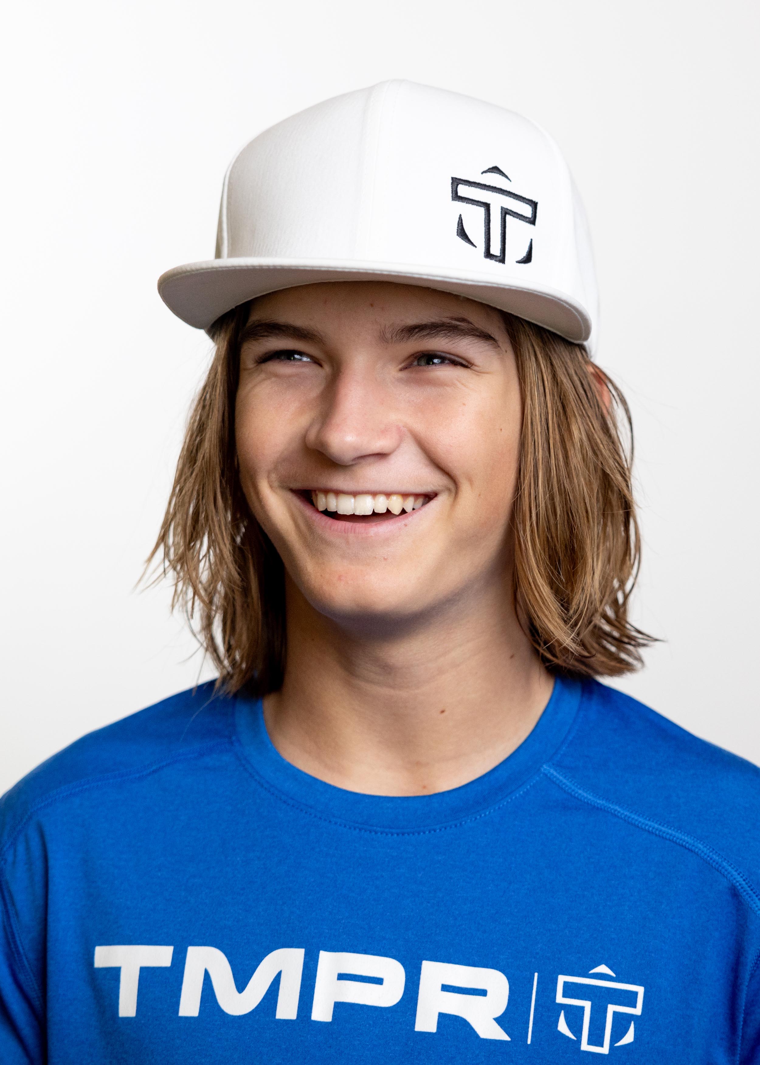 White flat bill cap by TMPR Sports featuring a black 'T' logo, worn by a smiling young person in a blue shirt.