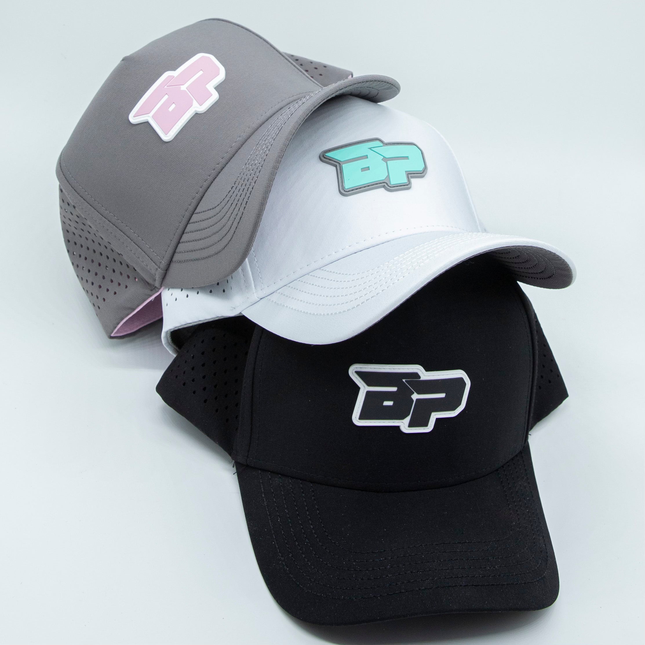 Three stacked baseball caps in gray, white, and black with "BP" logos.