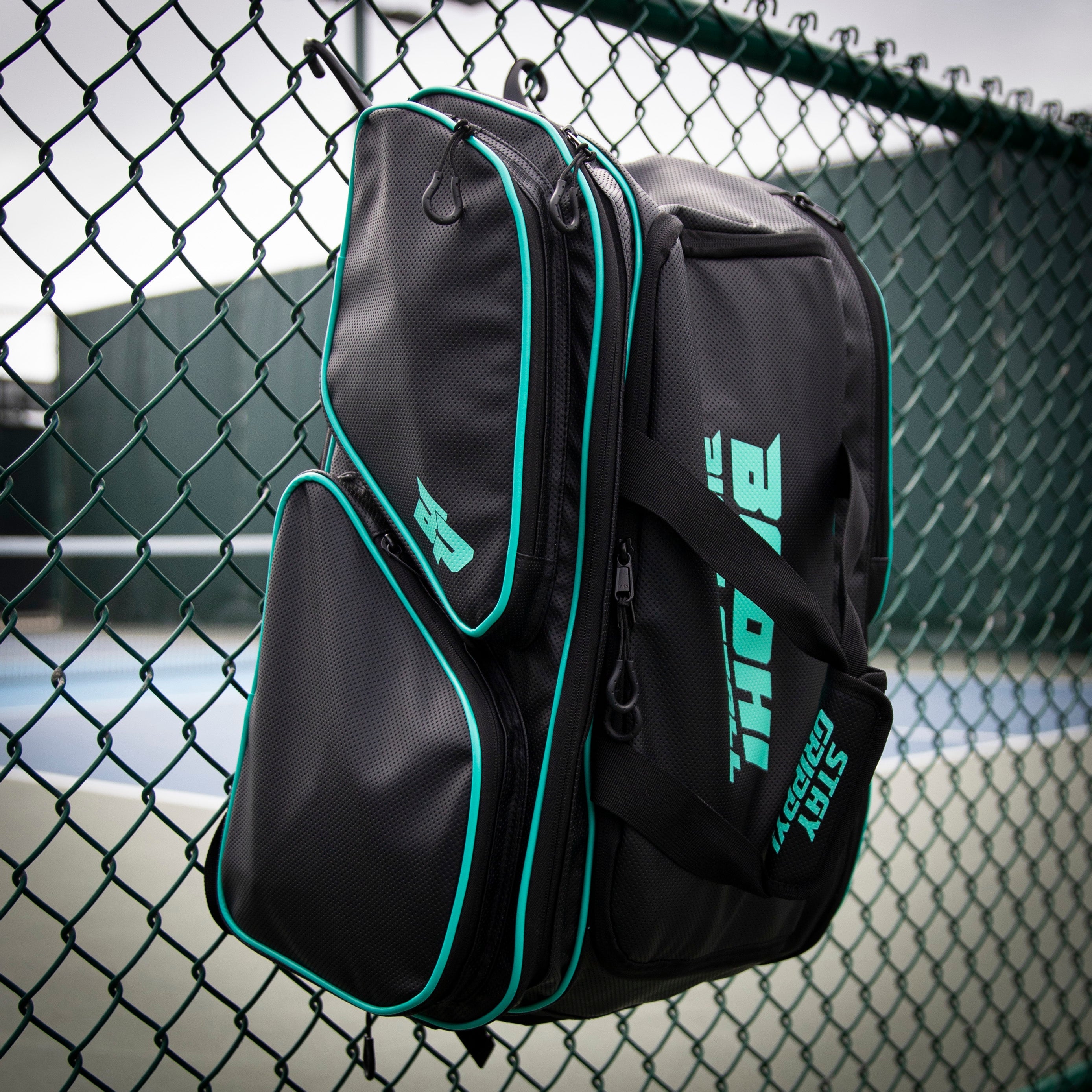 Black backpack with teal accents hanging on a green chain-link fence.