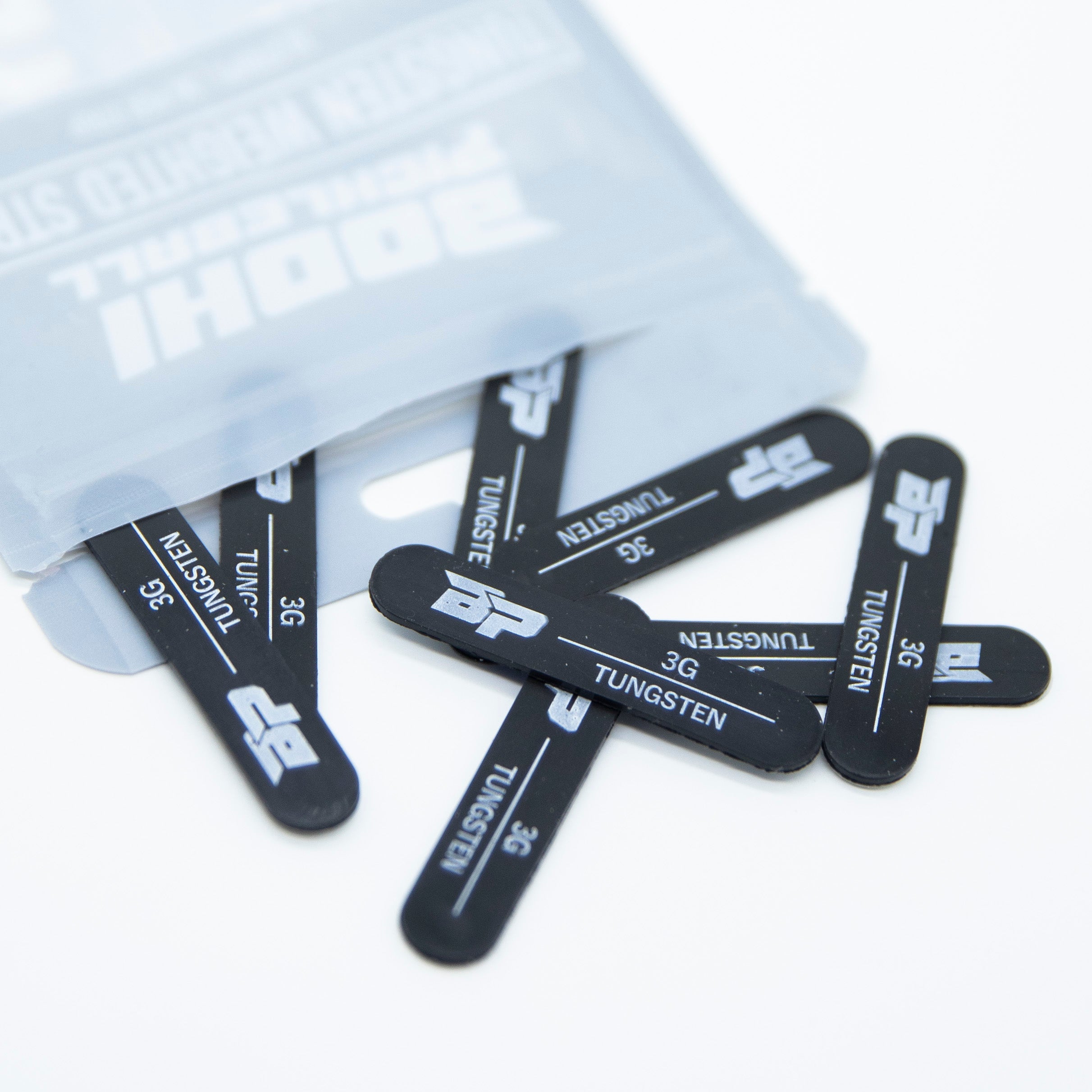 Scattered tungsten weighted strips beside an open Bodhi pickleball product bag.