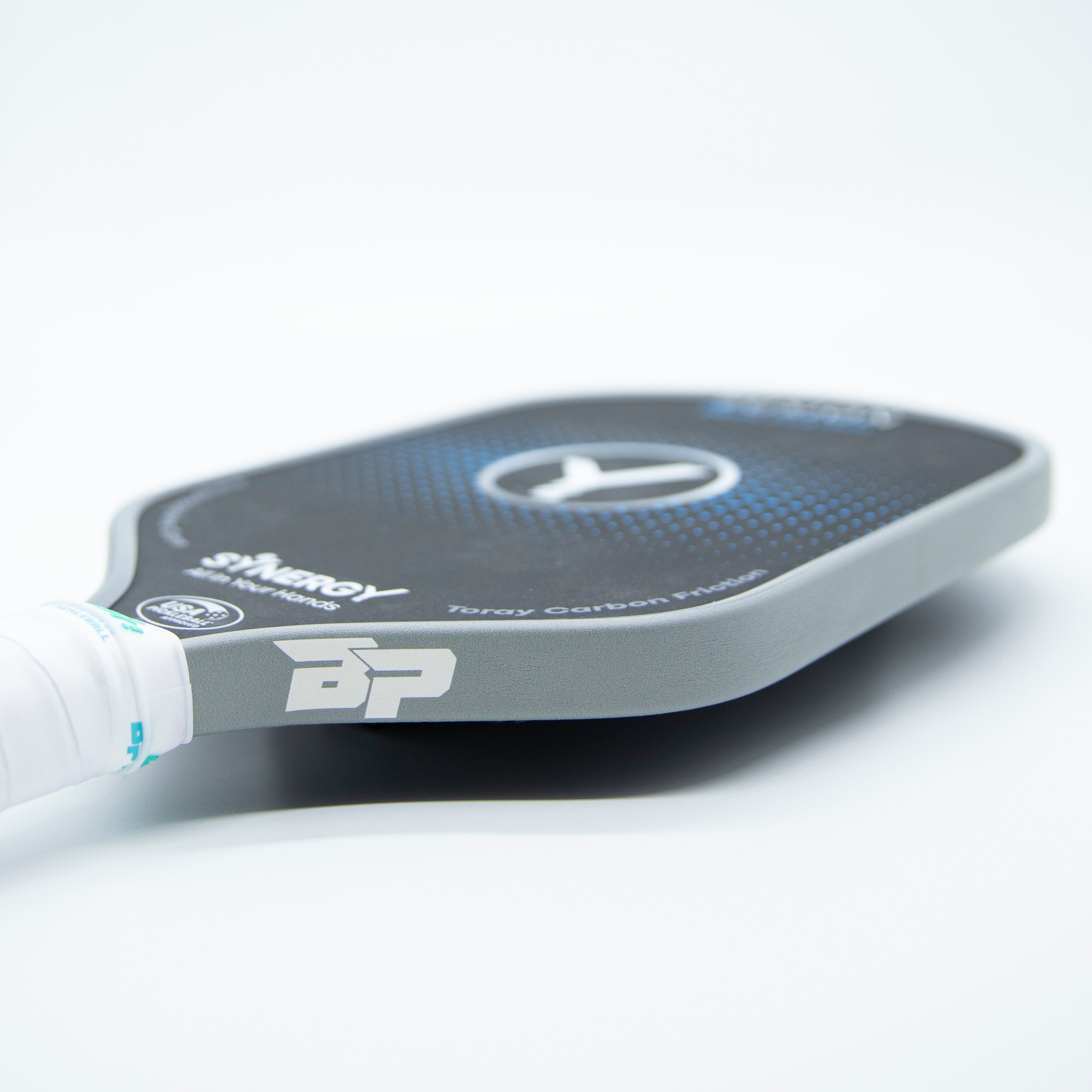 Grey pickleball paddle edge tape by DinkersAlley.com on a dark blue paddle with a white grip, cropped angled view.