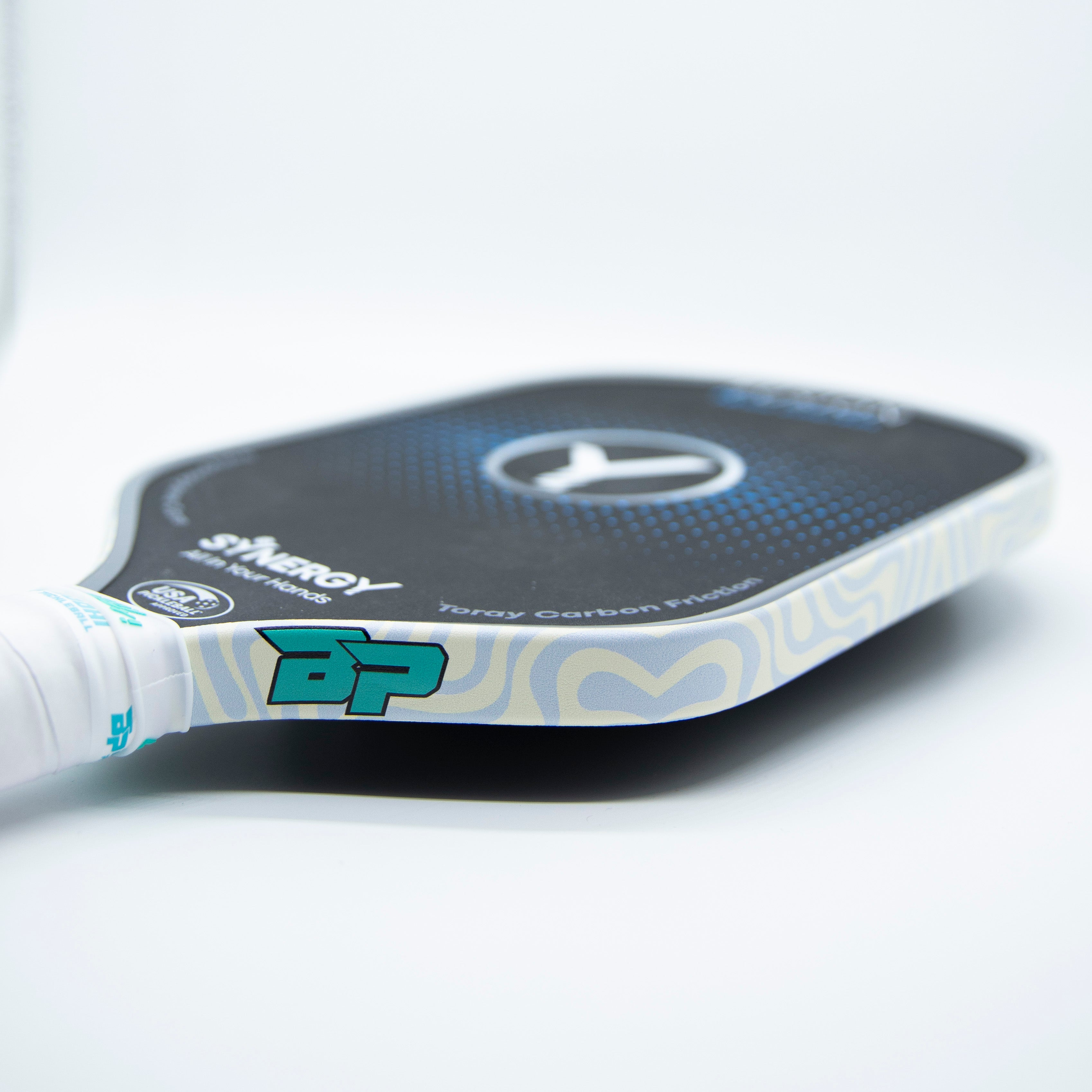 Close-up of a pickleball paddle with teal accents, white handle, and blue and white wave pattern around the edge.