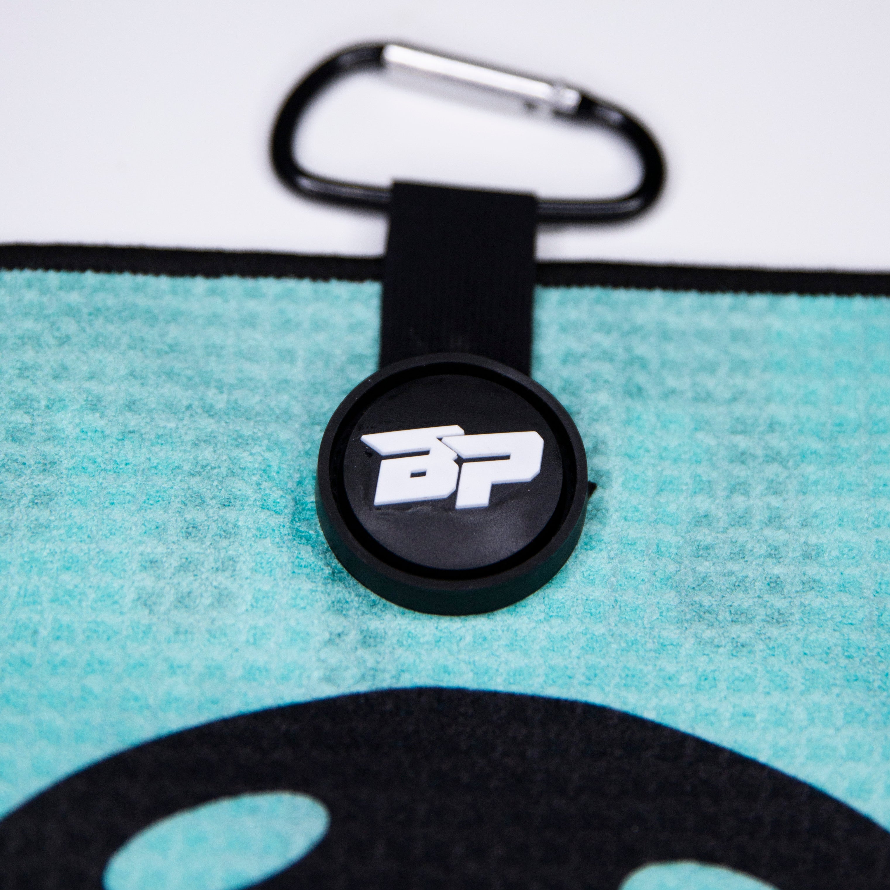 Close-up of an aqua-colored towel with a black logoed button and carabiner. 
