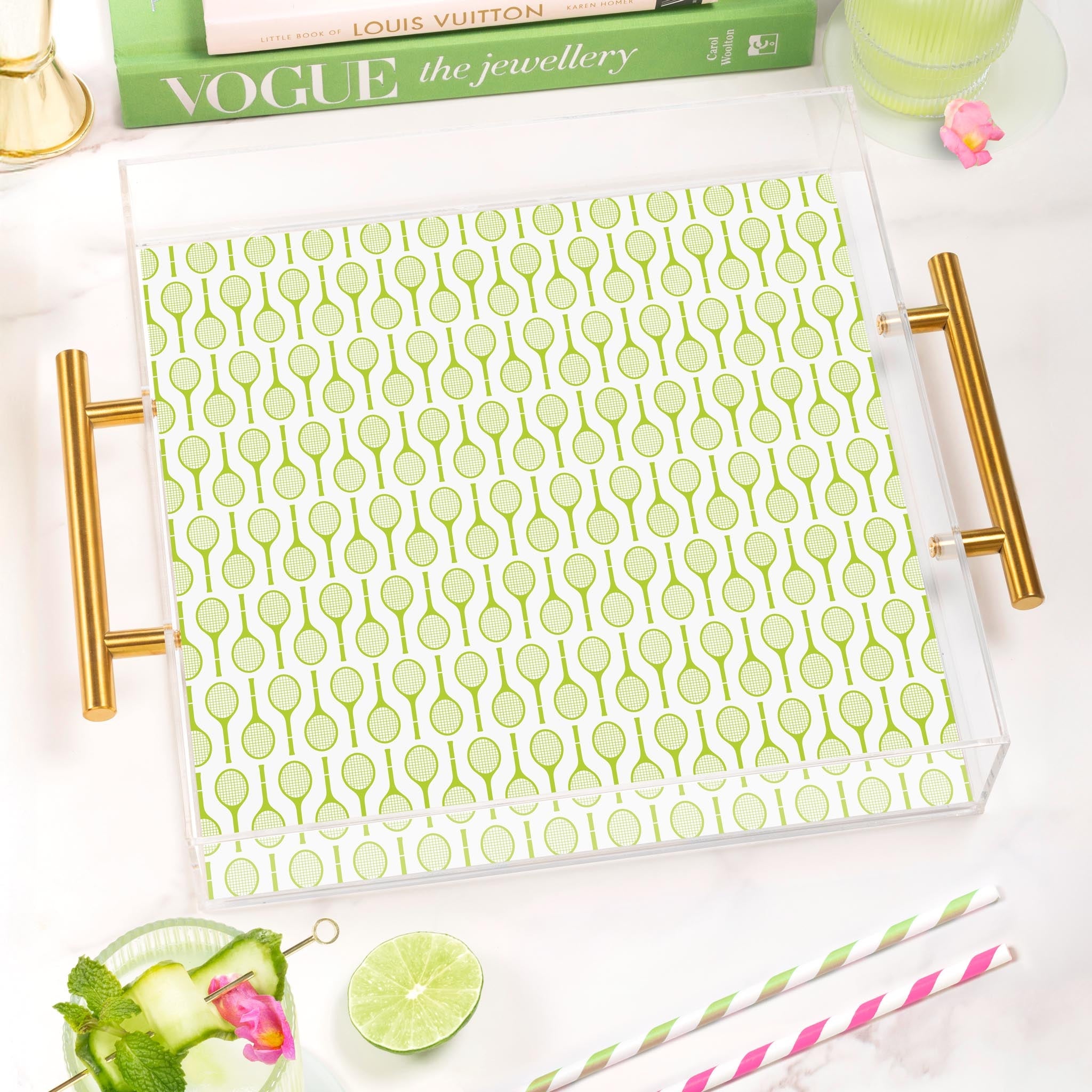 Acrylic serving tray with gold handles and a green tennis racket pattern on a white marble surface.