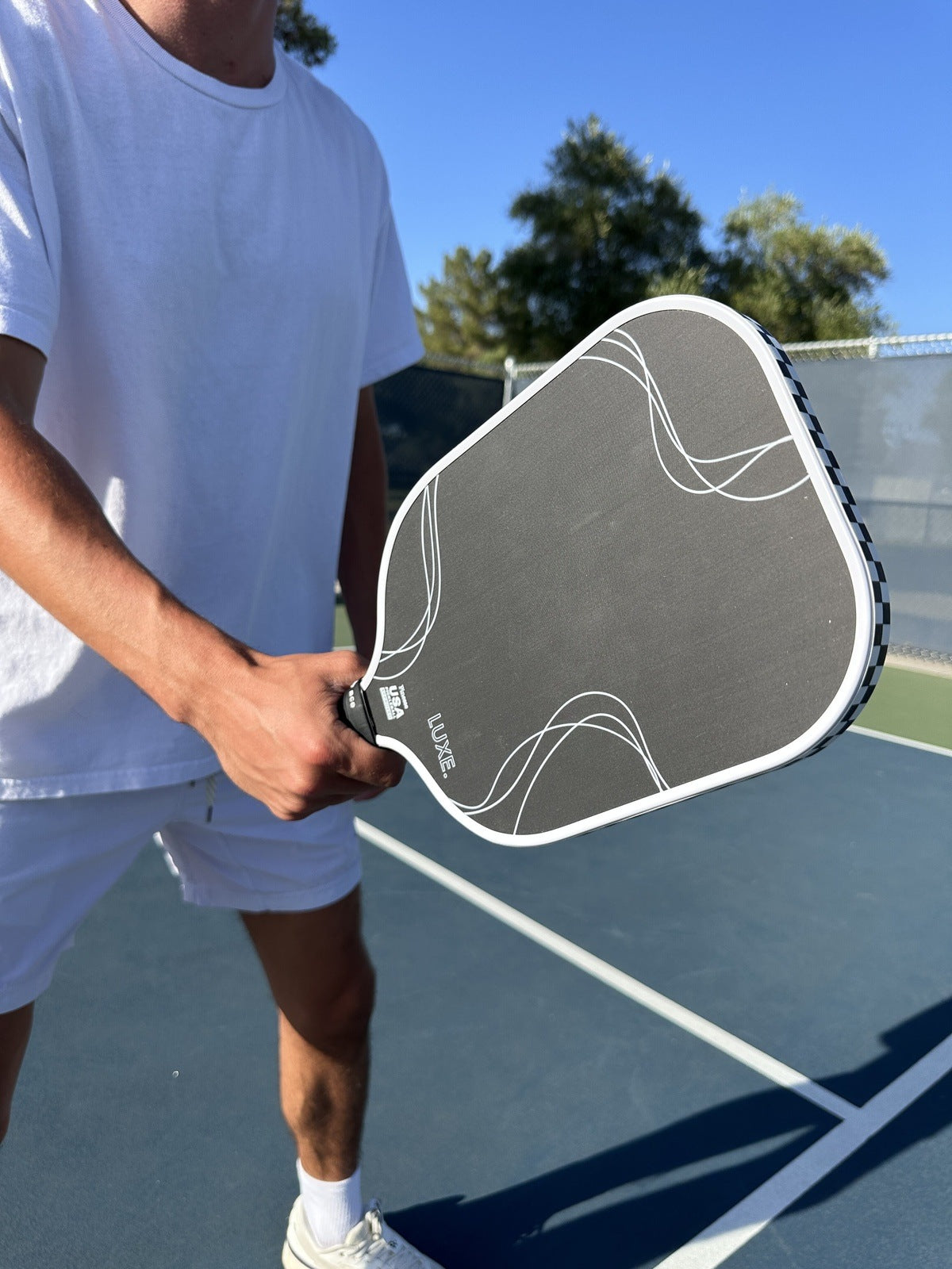 Man holding a black and white pickleball paddle on a blue court wearing white clothing.