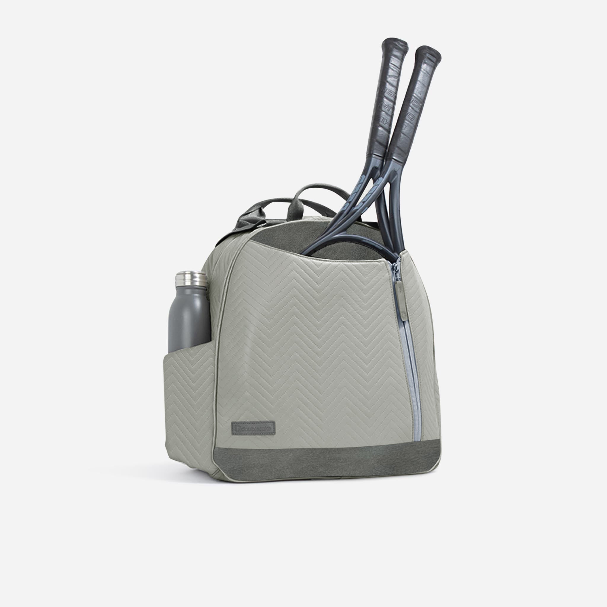 Light grey tennis backpack and tote by Doubletake, with a chevron pattern, holding a grey water bottle and two tennis rackets.